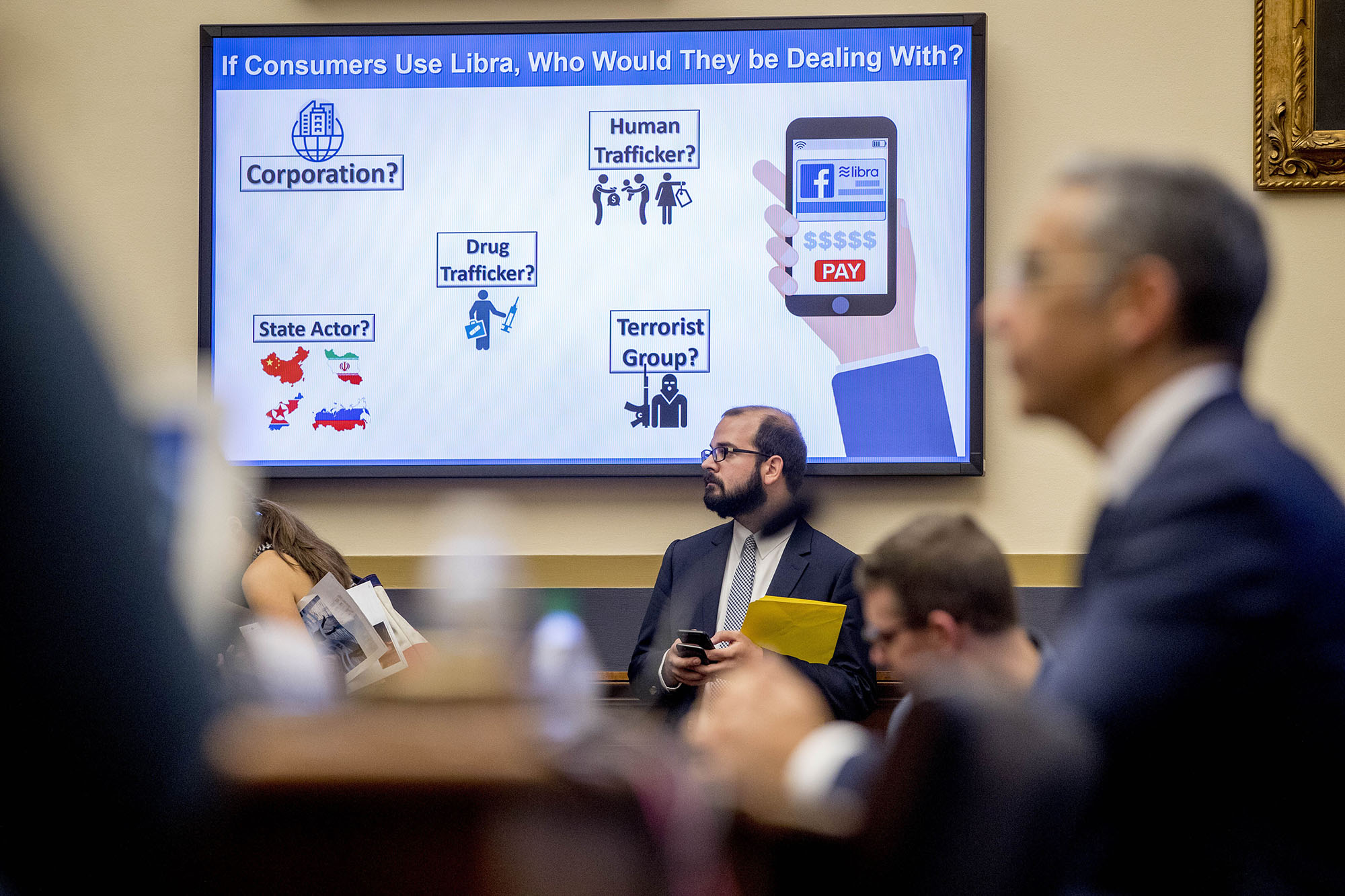 A big screen in the Congressional hearing room poses questions about Facebook&#039;s Libra.