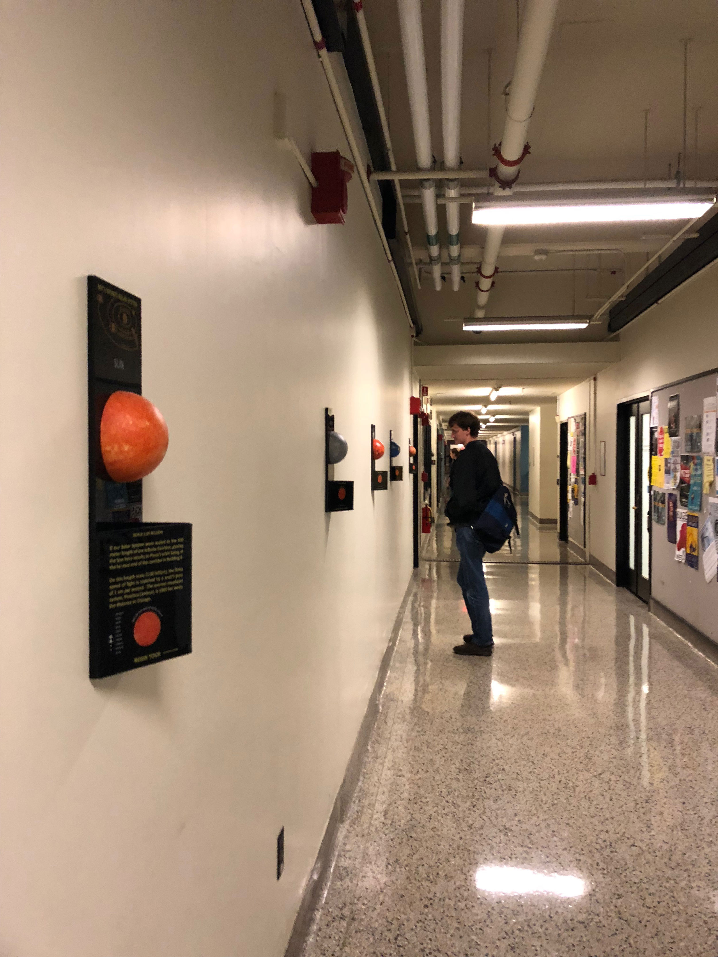Student standing in hallway looking at model planets and informational plaques on wall