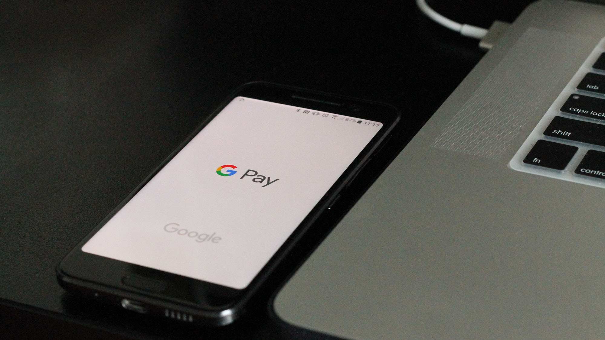 An image of a smartphone with the Google Pay application open on the screen, sitting next to a laptop computer.