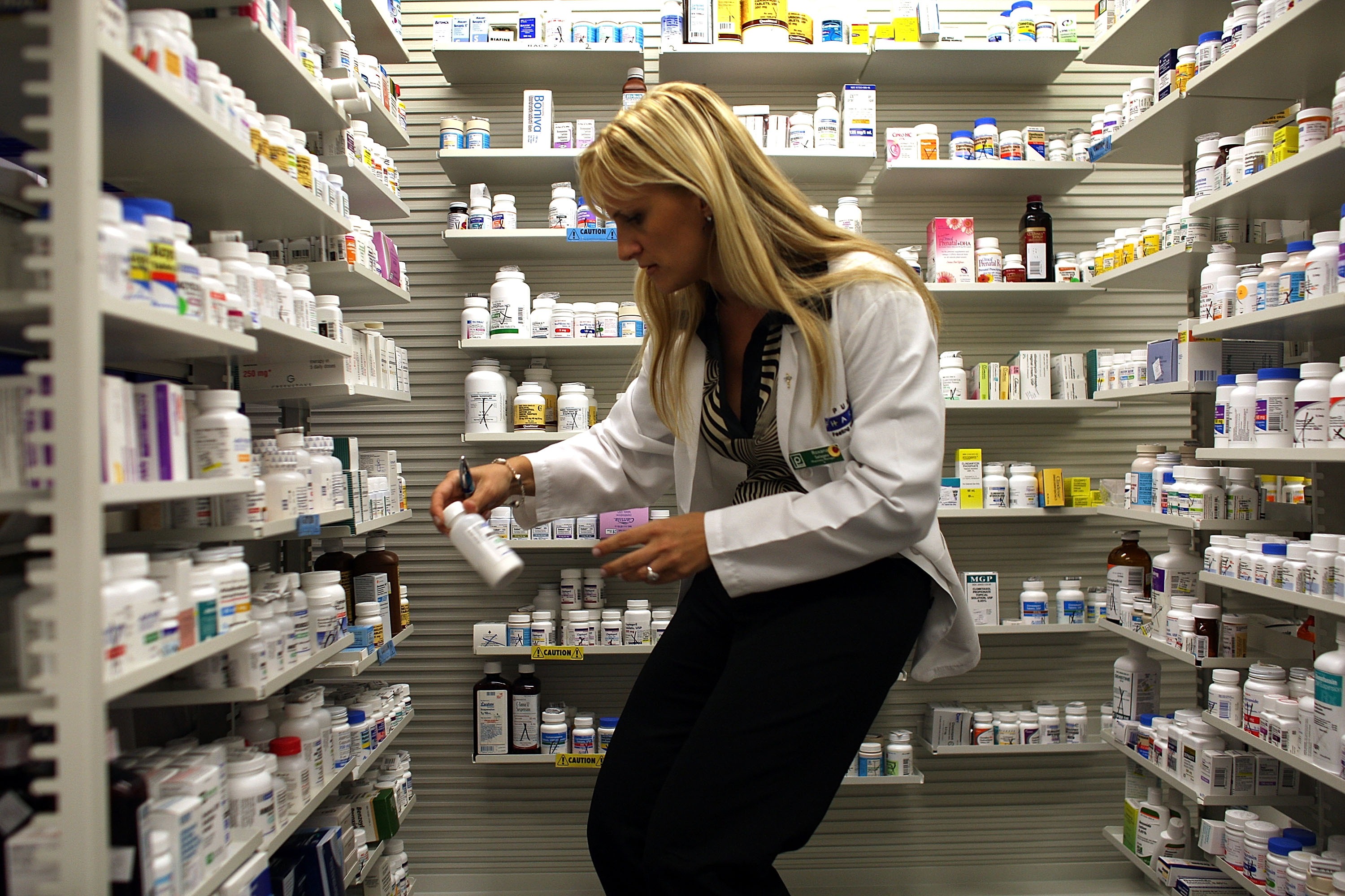 A pharmacist selects a bottle of medication from shelves and shelves of options.