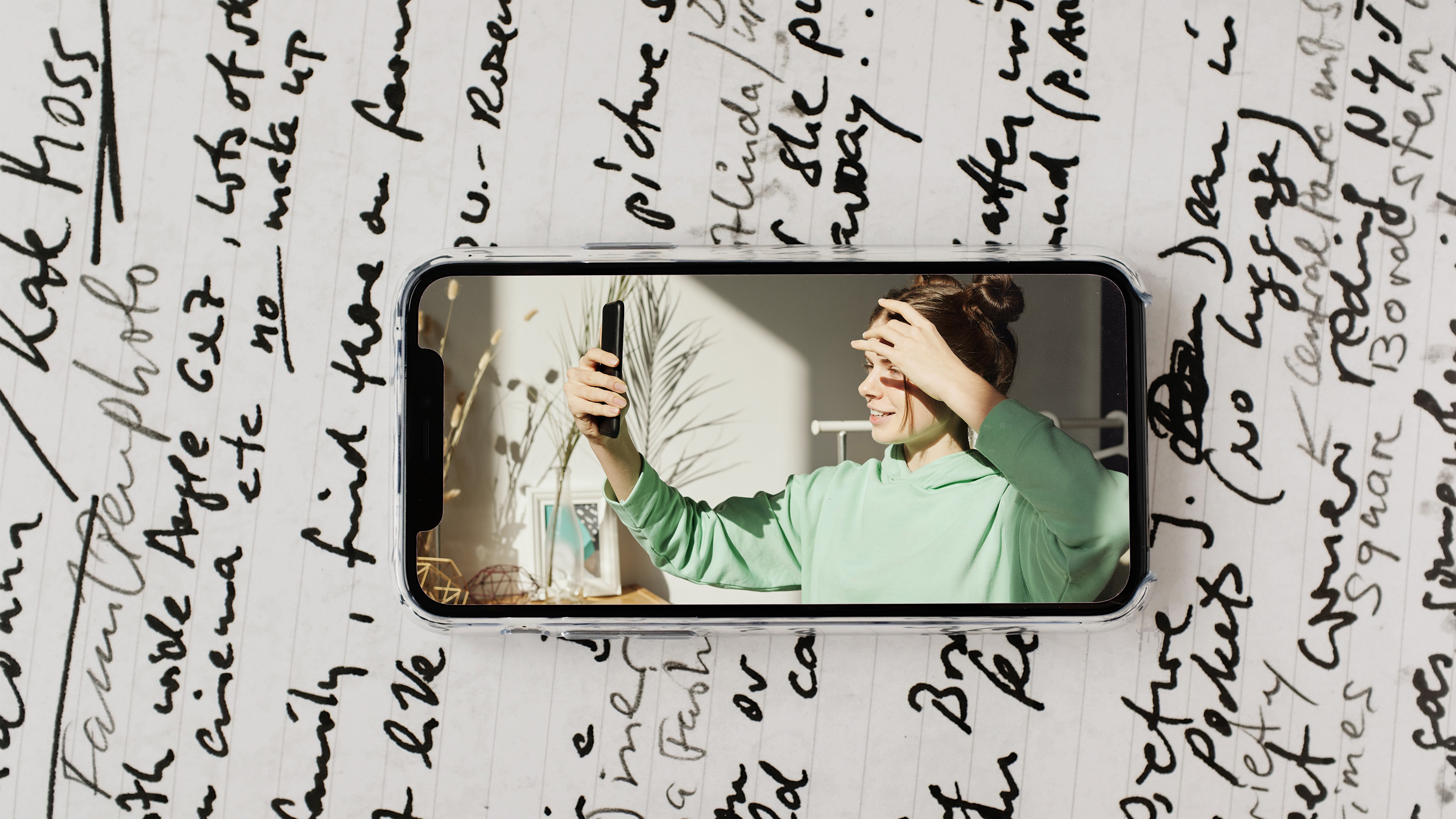 image of woman in green sweatshirt hoodie taking selfie with phone in apartment during coronavirus quarantine on phone with journal background isolation journal suleika jaouad