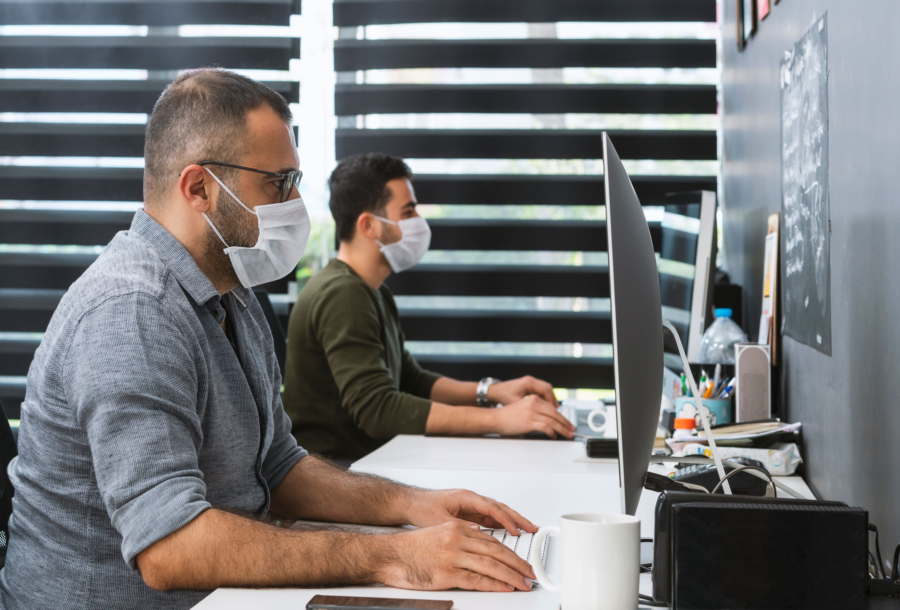 Two businessmen with protective face masks are working in the office