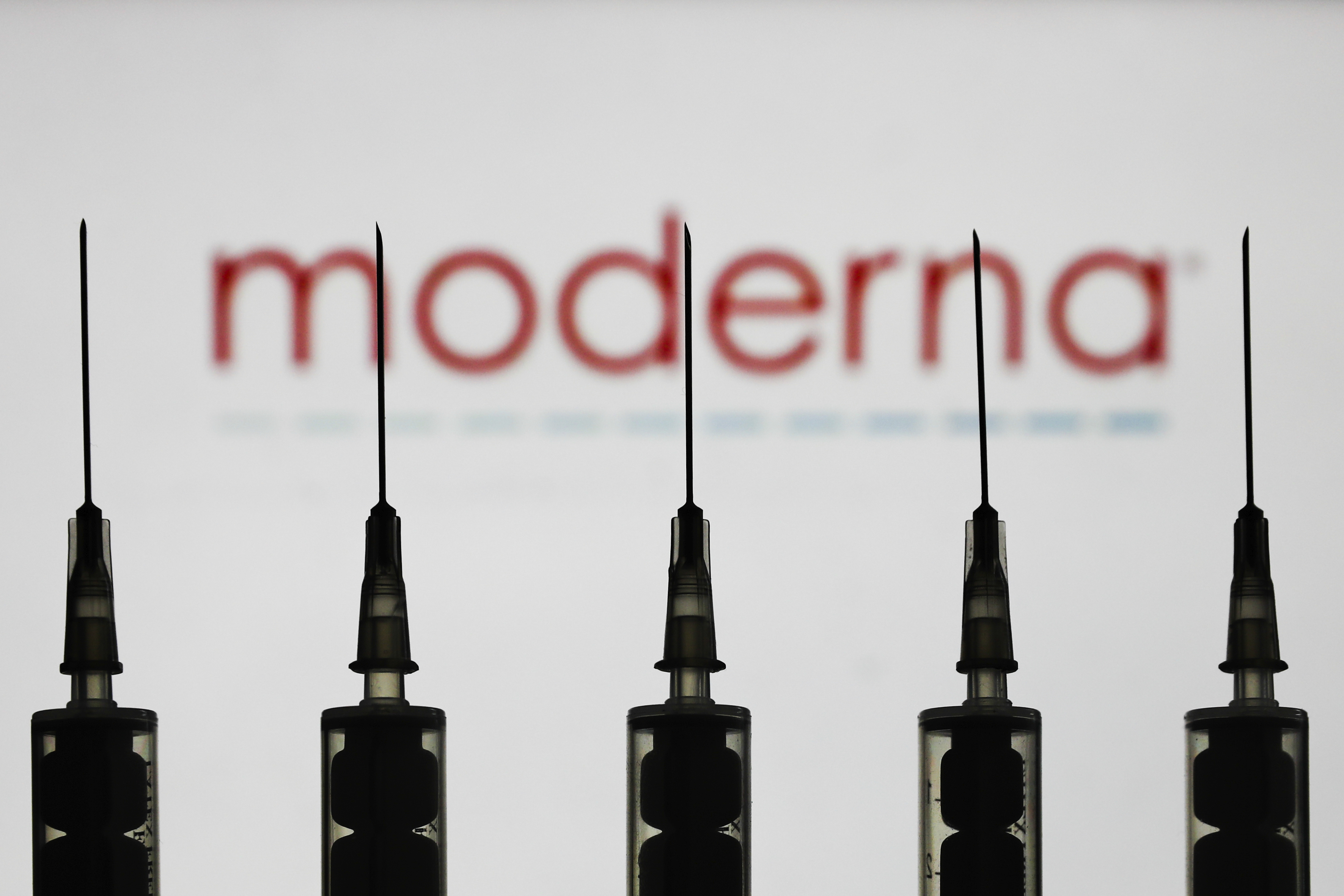 Medical syringes are seen with Moderna company logo displayed on a screen in the background in this illustration photo taken in Poland on October 12, 2020. (Photo illustration by Jakub Porzycki/NurPhoto via AP)