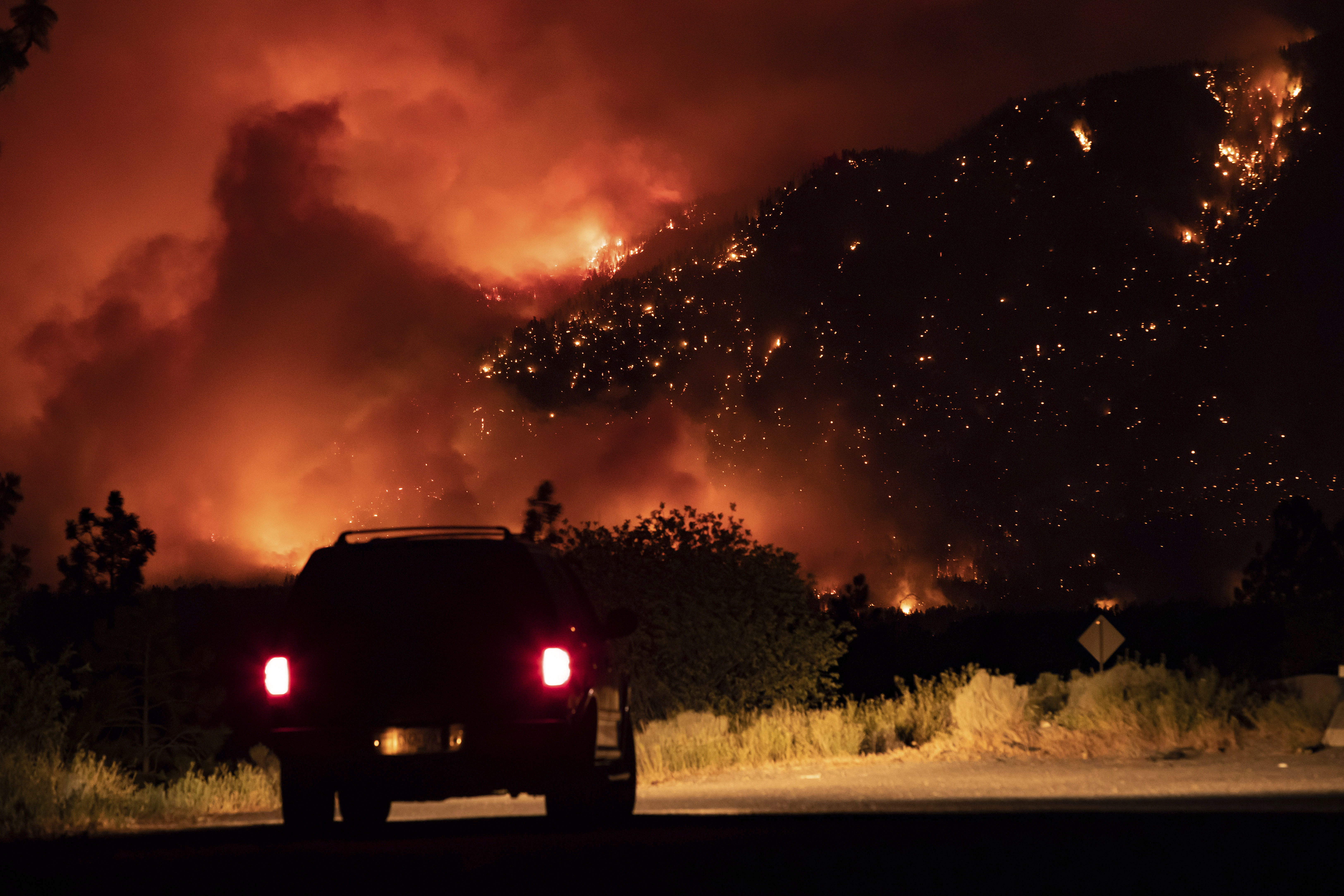 A motorist watches from a pullout on the Trans-Canada Highway as a wildfire burns on the side of a mountain in Lytton, B.C., Thursday, July 1, 2021. (Darryl Dyck/The Canadian Press via AP)