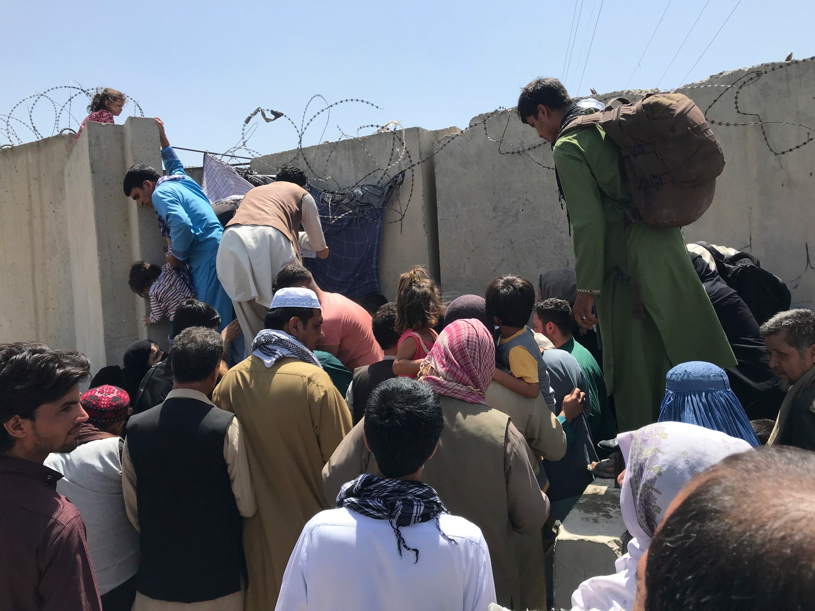 People struggle to cross the boundary wall of Hamid Karzai International Airport in Kabul.