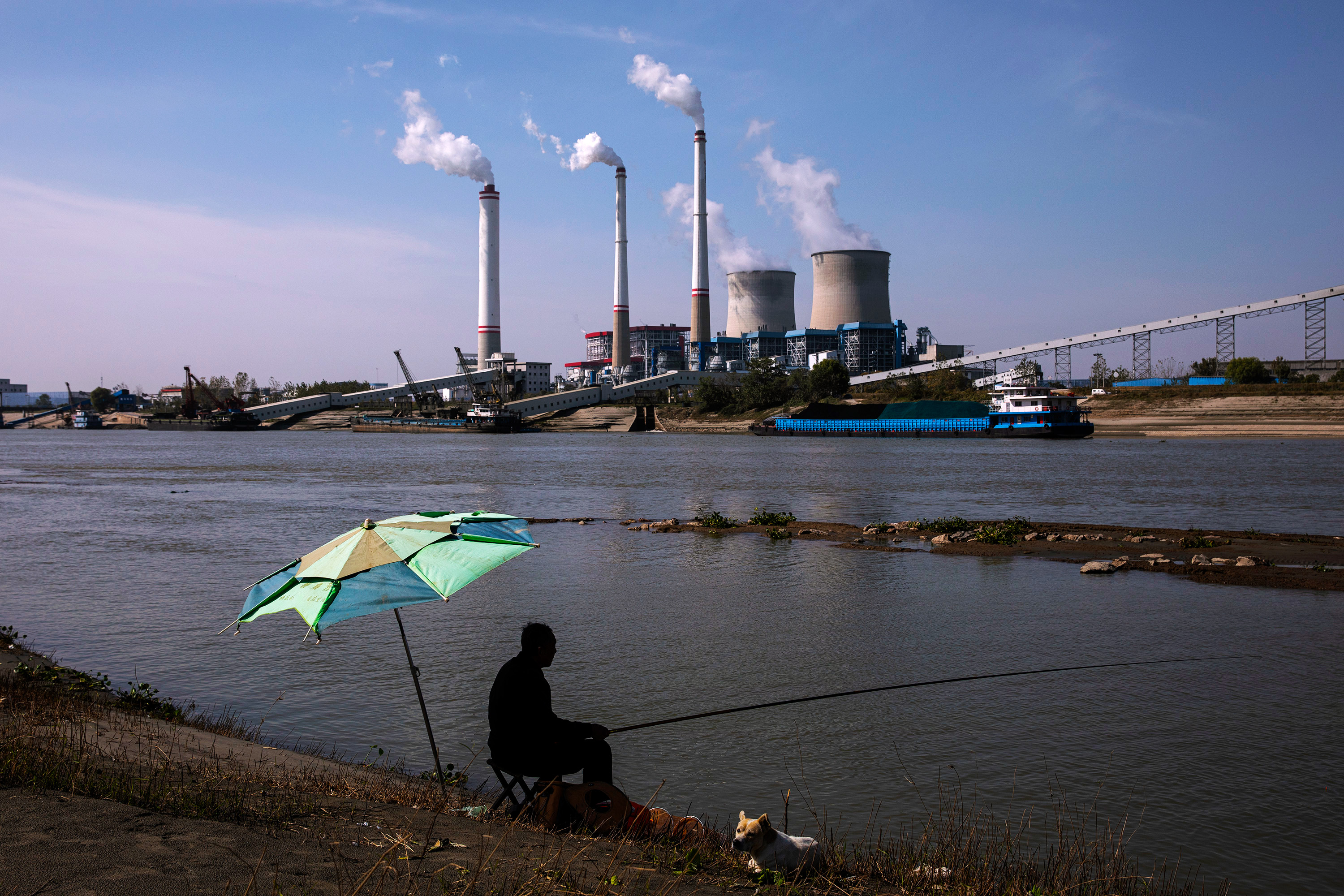 Resident sits by the river fishing as coal fired power plant