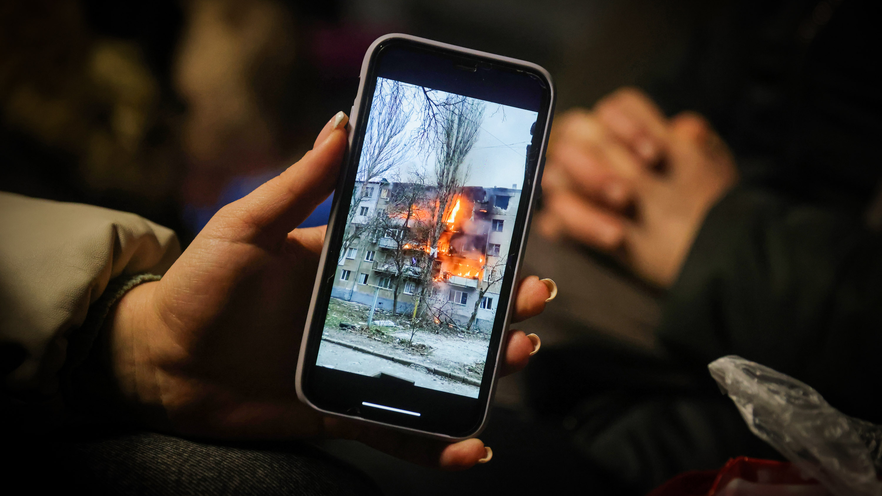 hand holding smartphone with a video of an apartment block in Mykolaiv on fire following a Russian attack