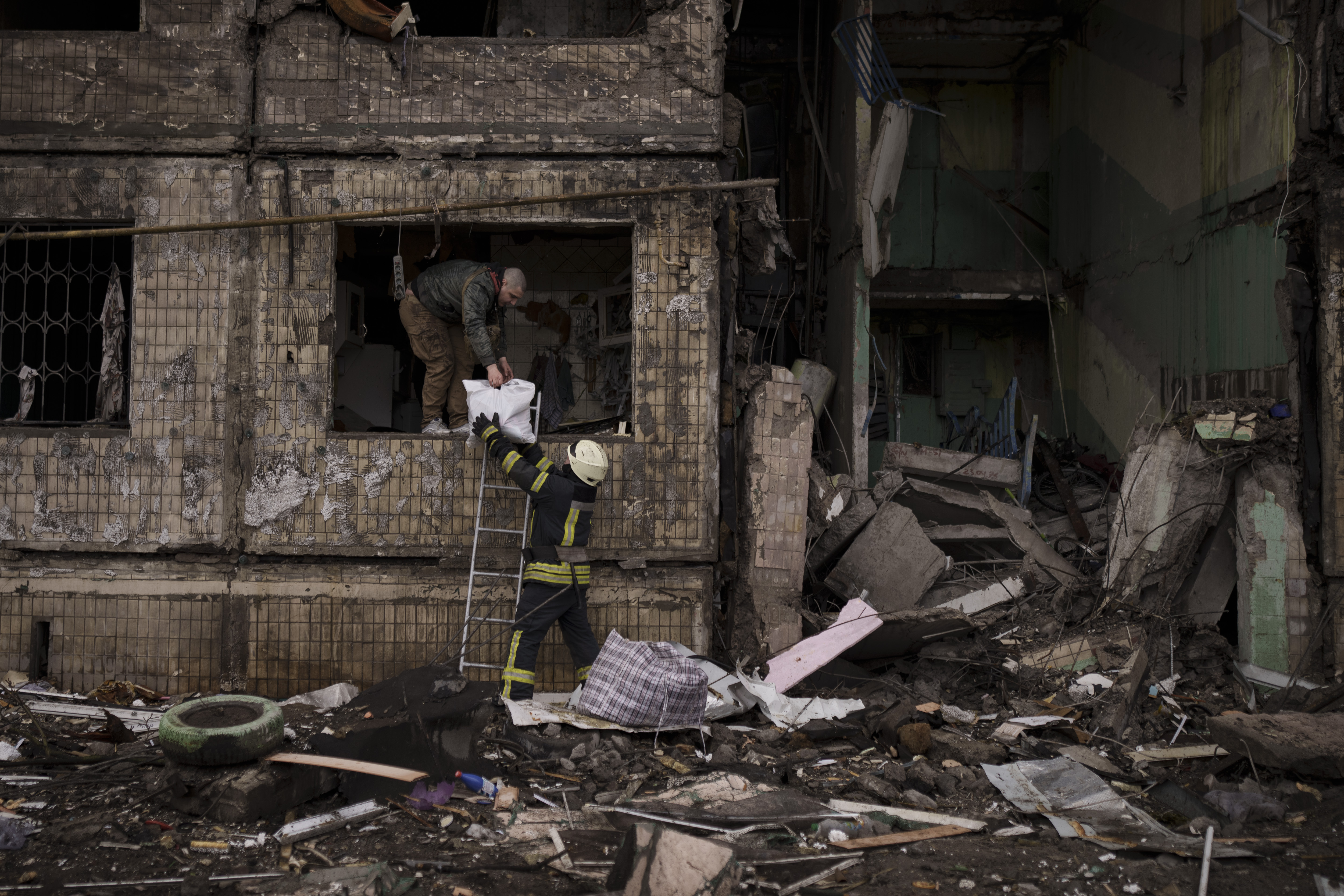 A Ukrainian firefighter helps a man remove belongings from a destroyed building after it was hit by artillery shelling in Kyiv in Kyiv, Ukraine, Monday, March 14, 2022. (AP Photo/Felipe Dana)