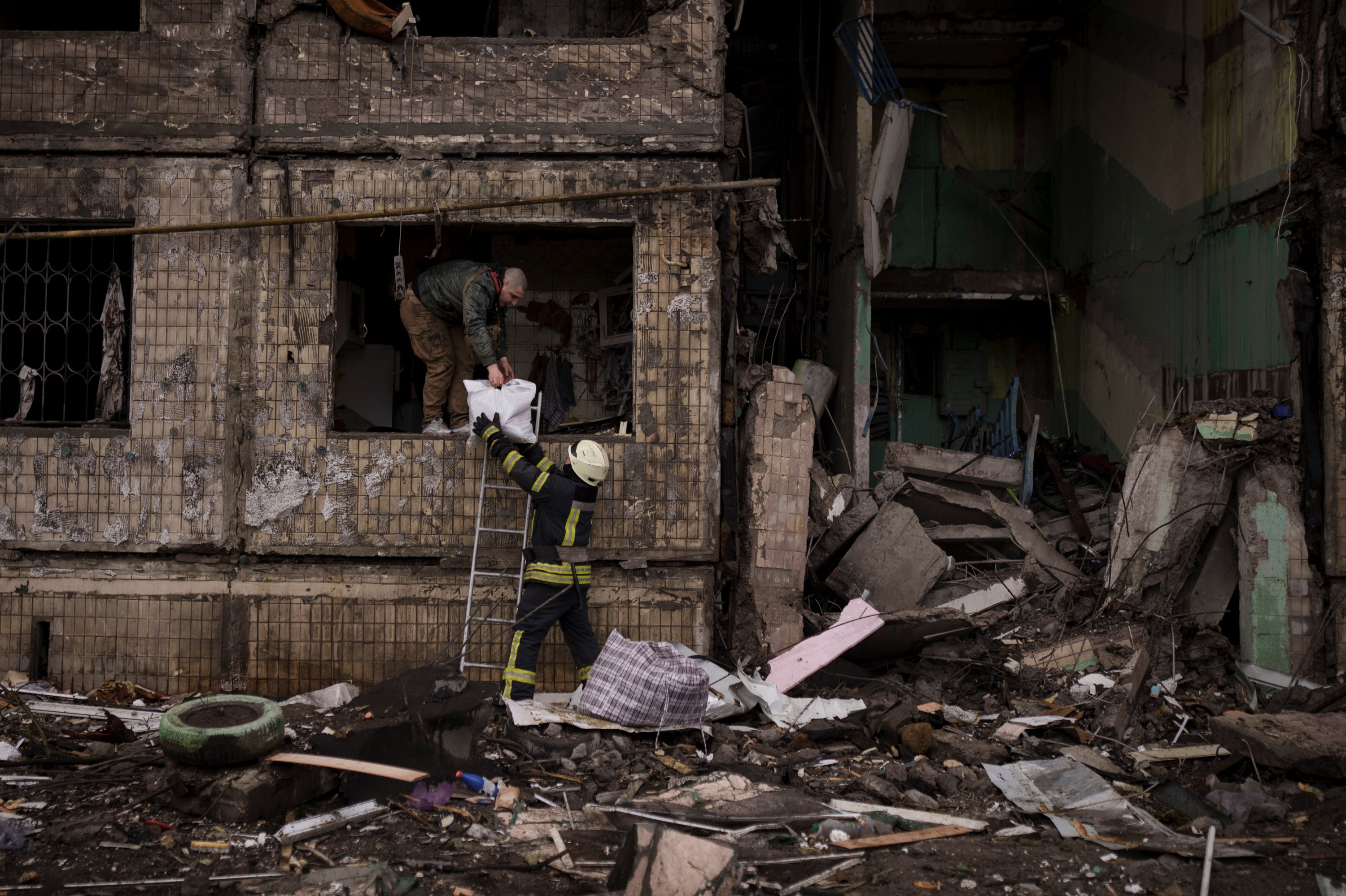 A Ukrainian firefighter helps a man remove belongings from a destroyed building after it was hit by artillery shelling in Kyiv in Kyiv, Ukraine, Monday, March 14, 2022. (AP Photo/Felipe Dana)