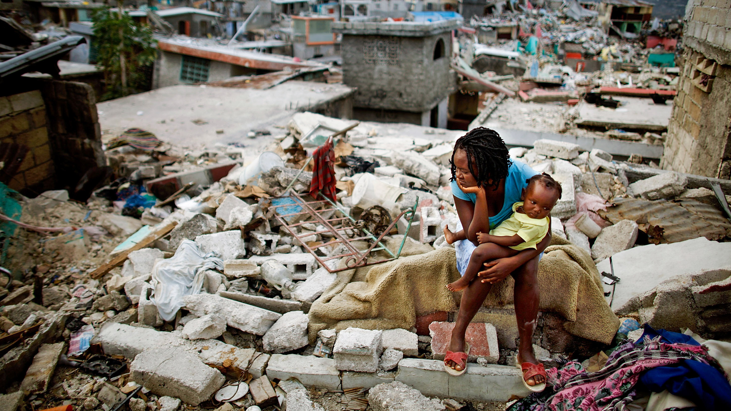 Sherider Anilus, 28, and her daughter, 9-month-old Monica, sit on the spot where her home collapsed