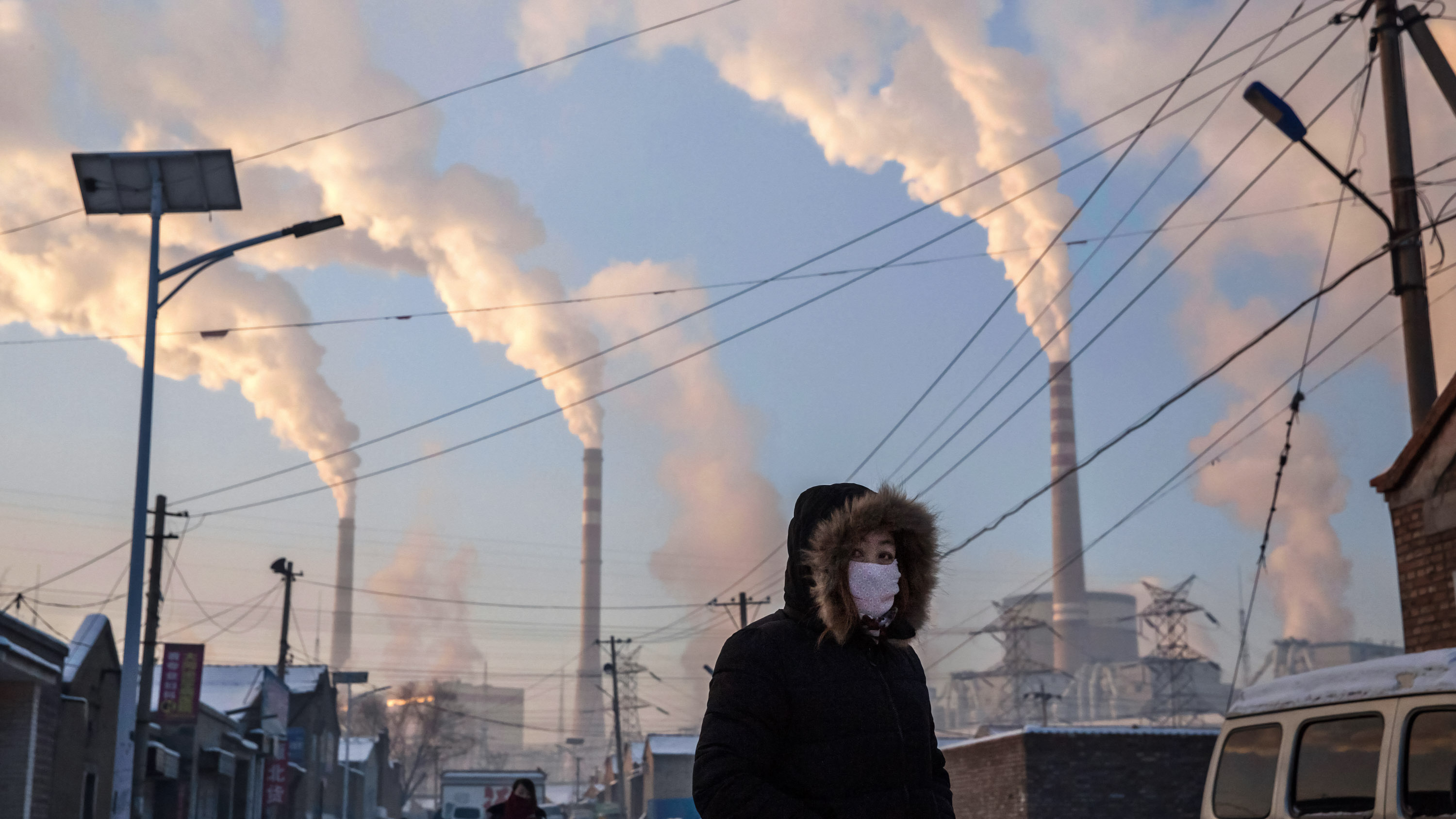 masked woman walks in neighborhood near a coal fired power plant
