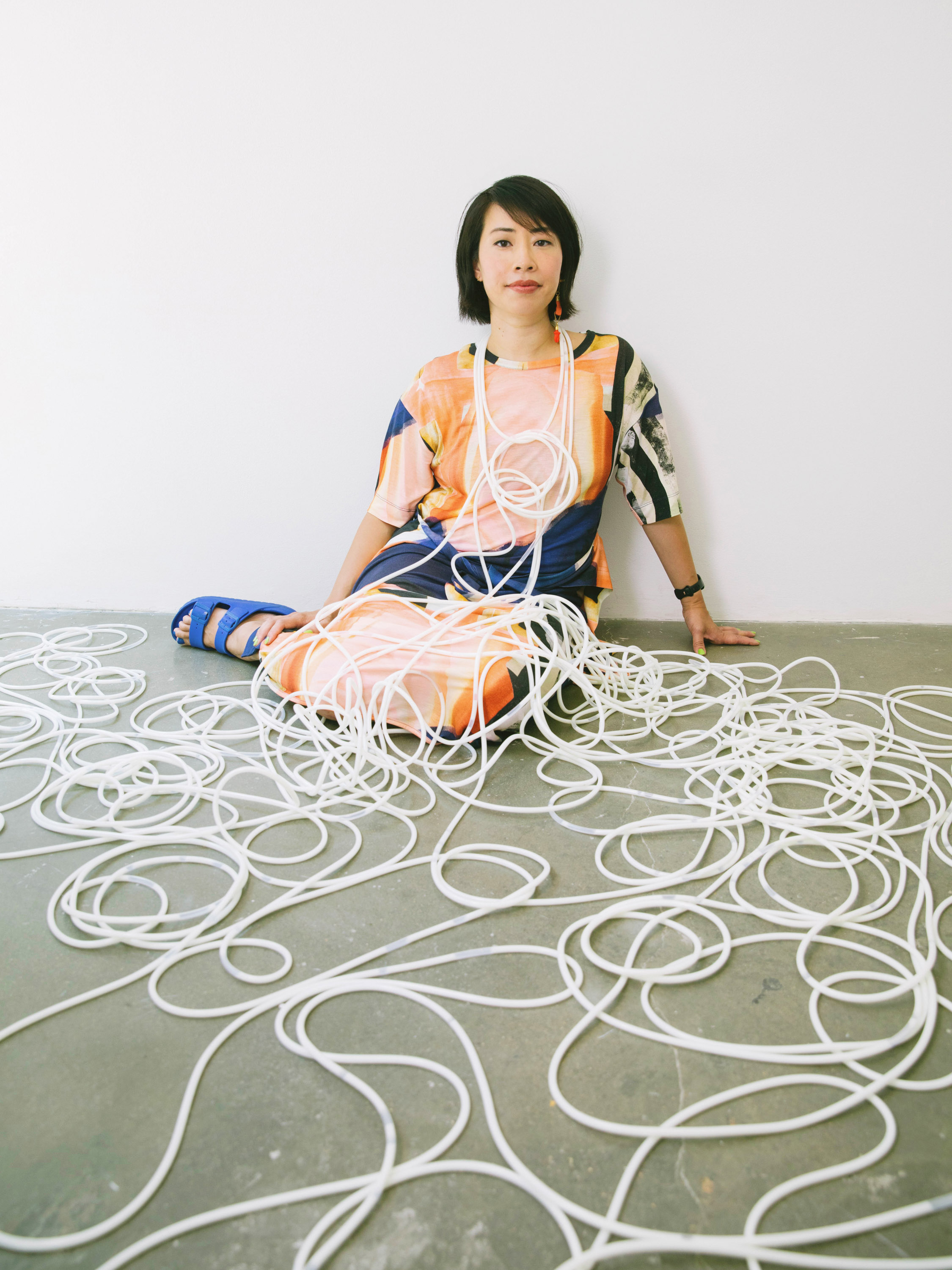 Ani Liu sitting on the gallery floor covered and surrounded by tubing