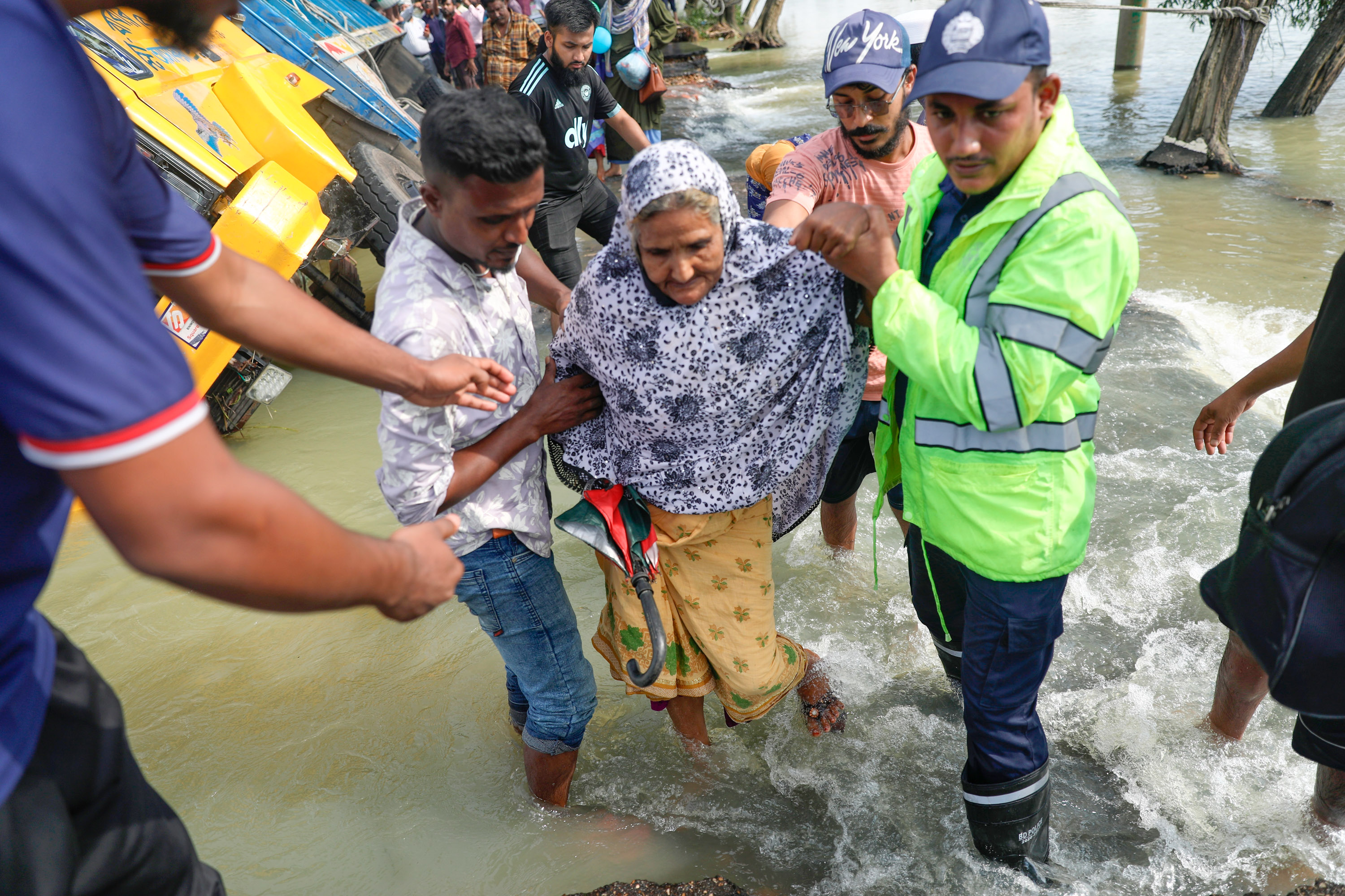 La gente pasa junto a camiones varados en una calle inundada en Sunamganj, Sylhet, Bangladesh, el 22 de junio de 2022.