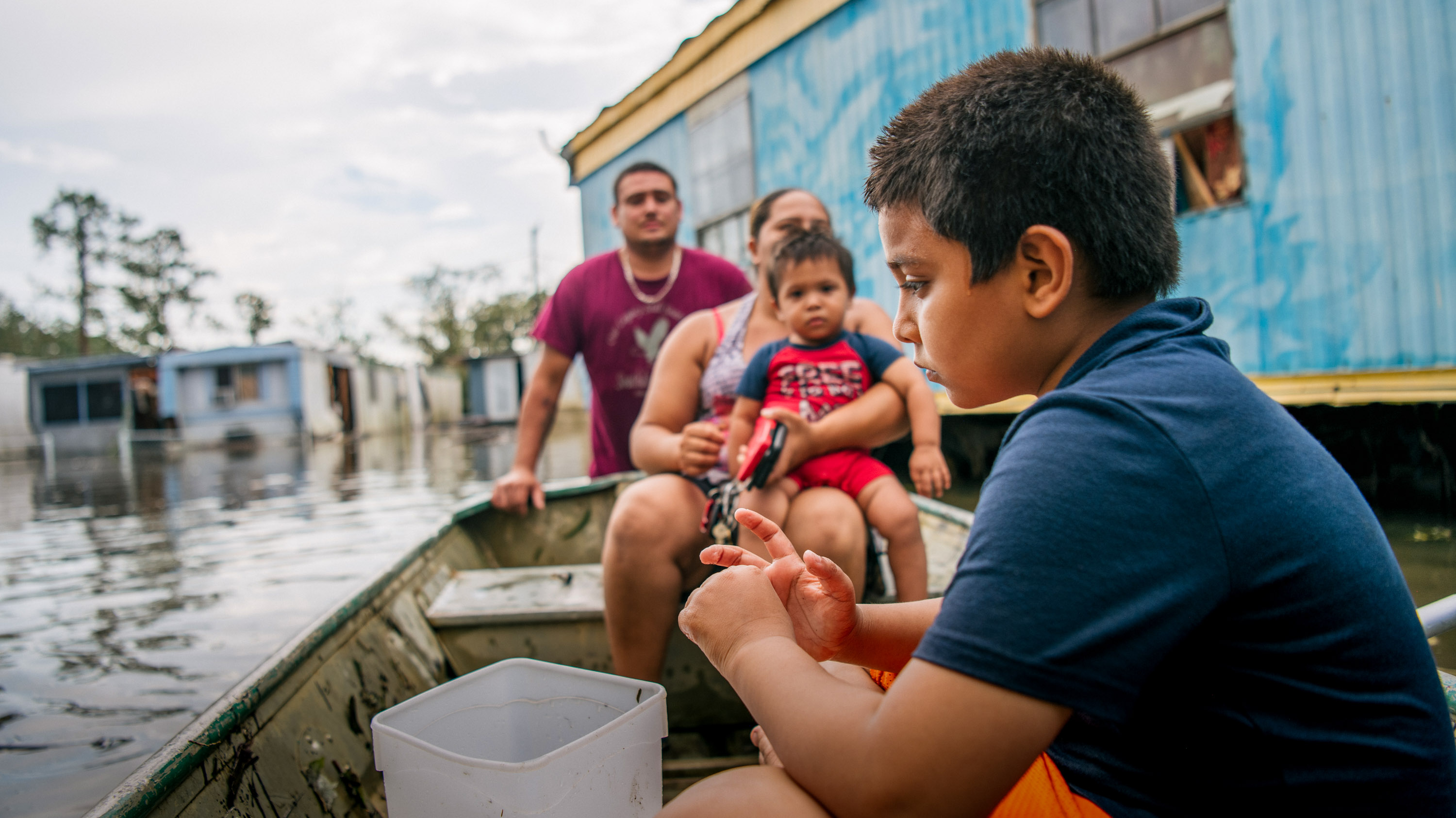 Father and his two small children in a boat surrounded by flooded homes