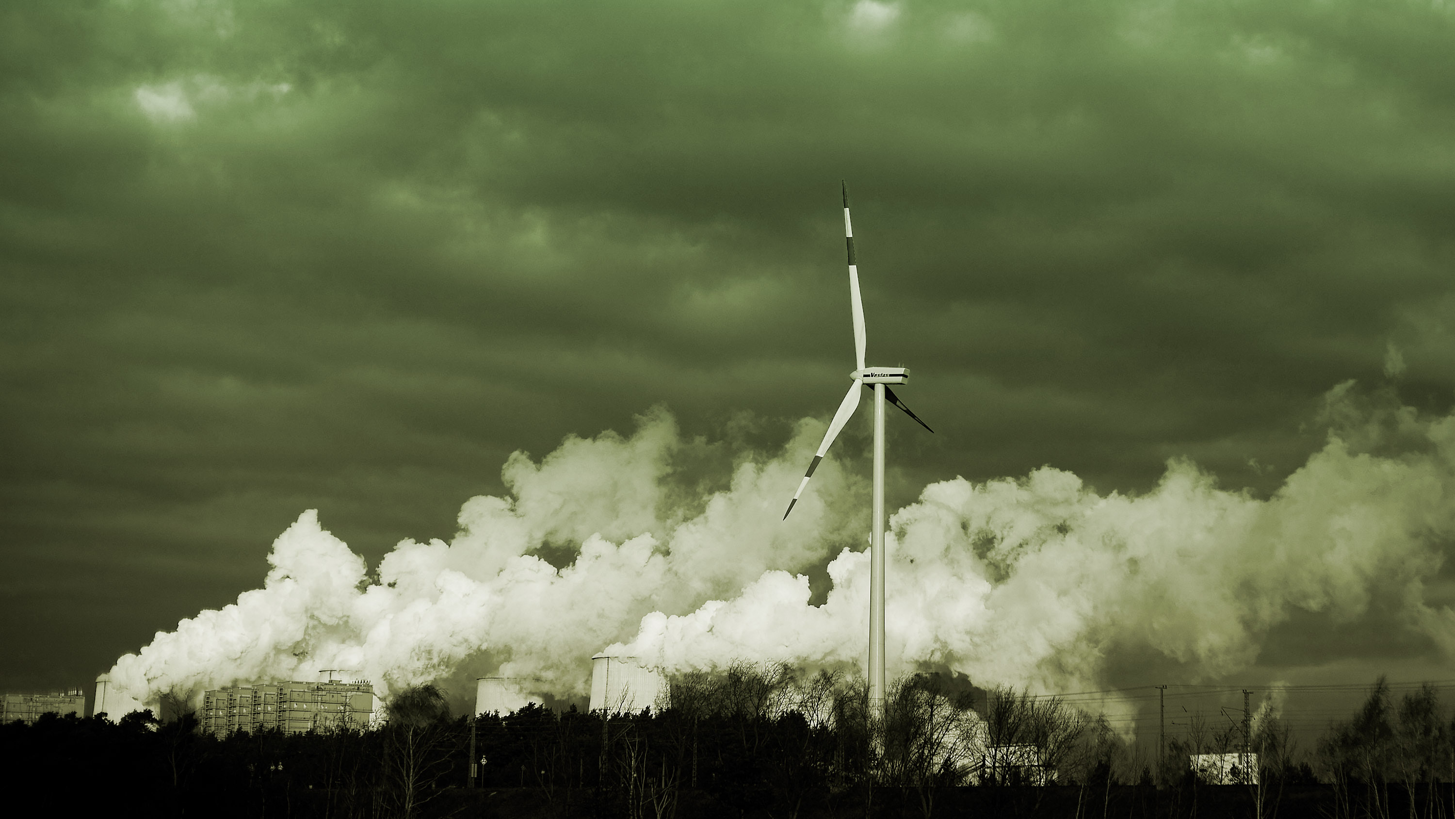a single wind turbine spins next to exhaust from a coal-fired industrial plant