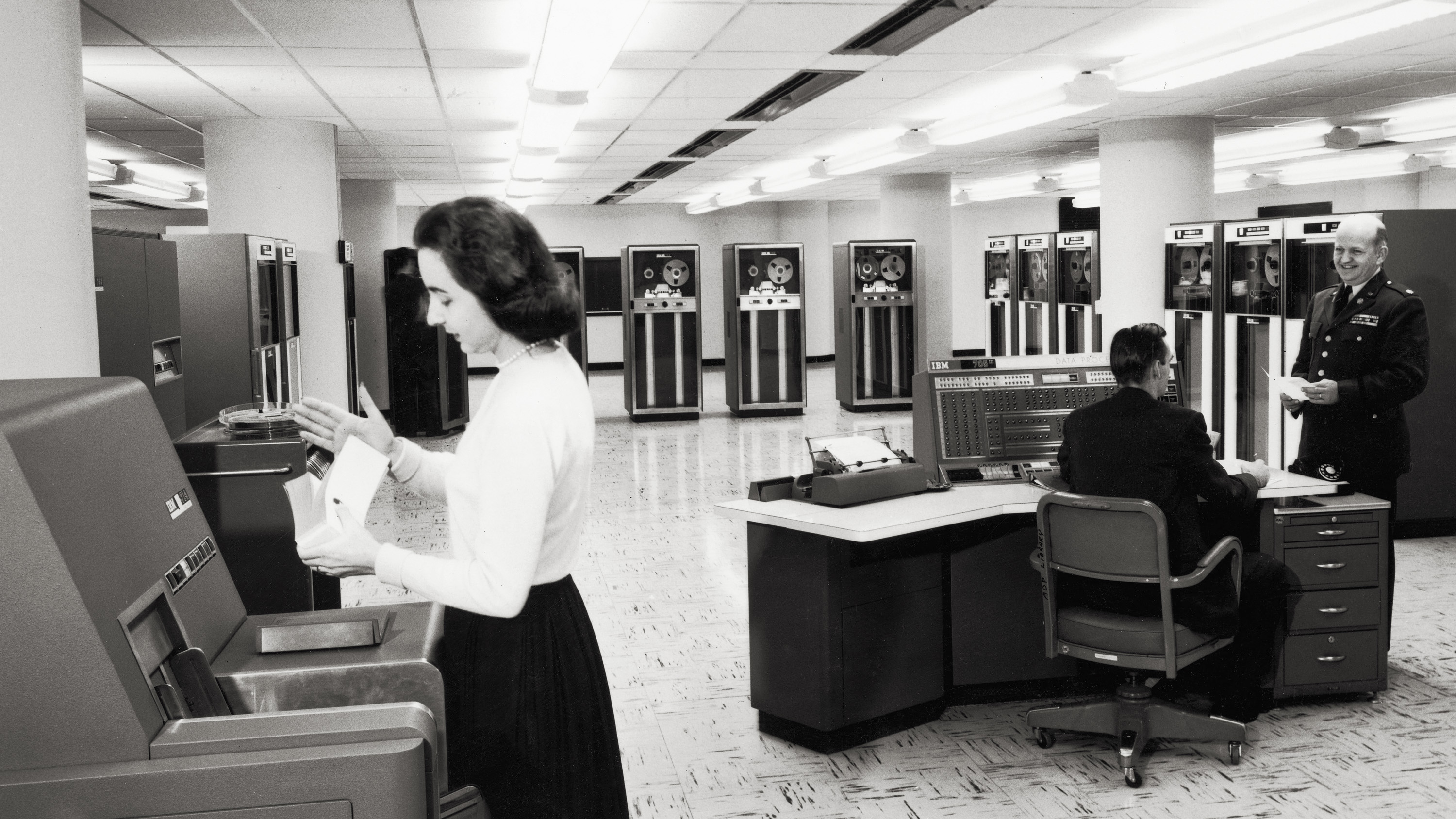 Arbeiterin im Vordergrund eines Raums mit Computern aus den 1950er Jahren