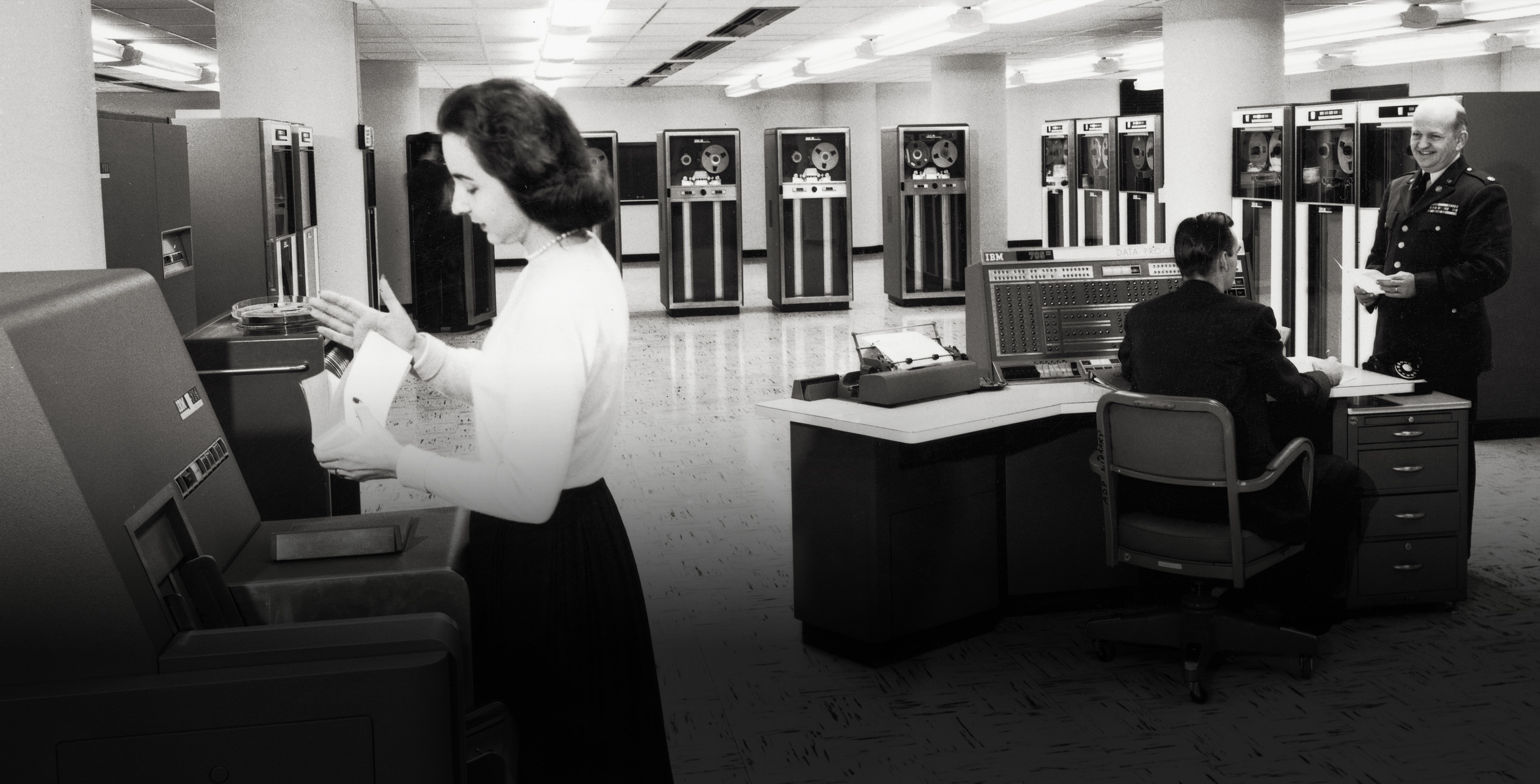 Circa 1955, a female office worker sorts punch cards as two men talk near the console of an IBM 705 III mainframe computer, owned by the US Army.