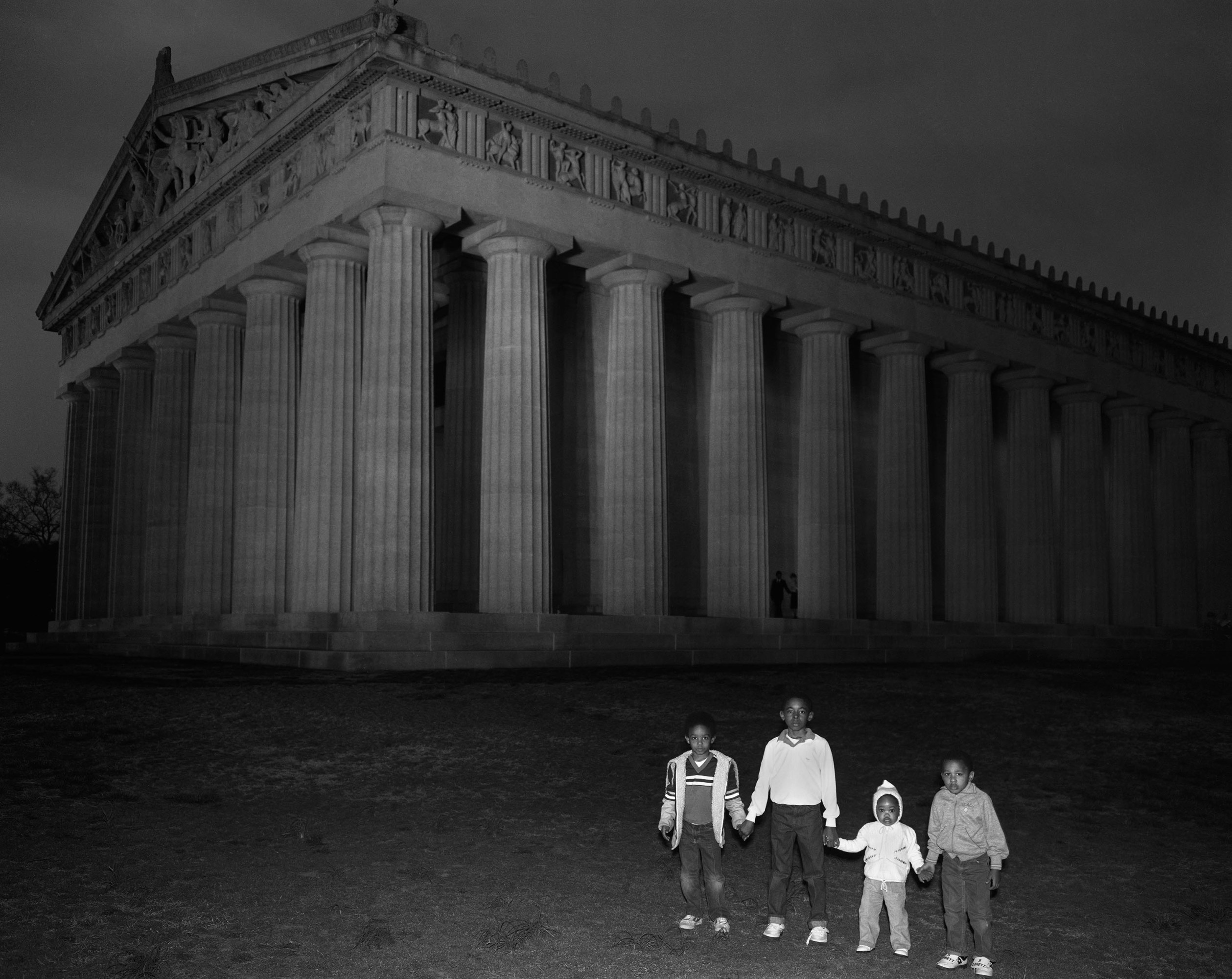A strong flash lights four children hold hands in front of the darkened Parthenon in Nashville.