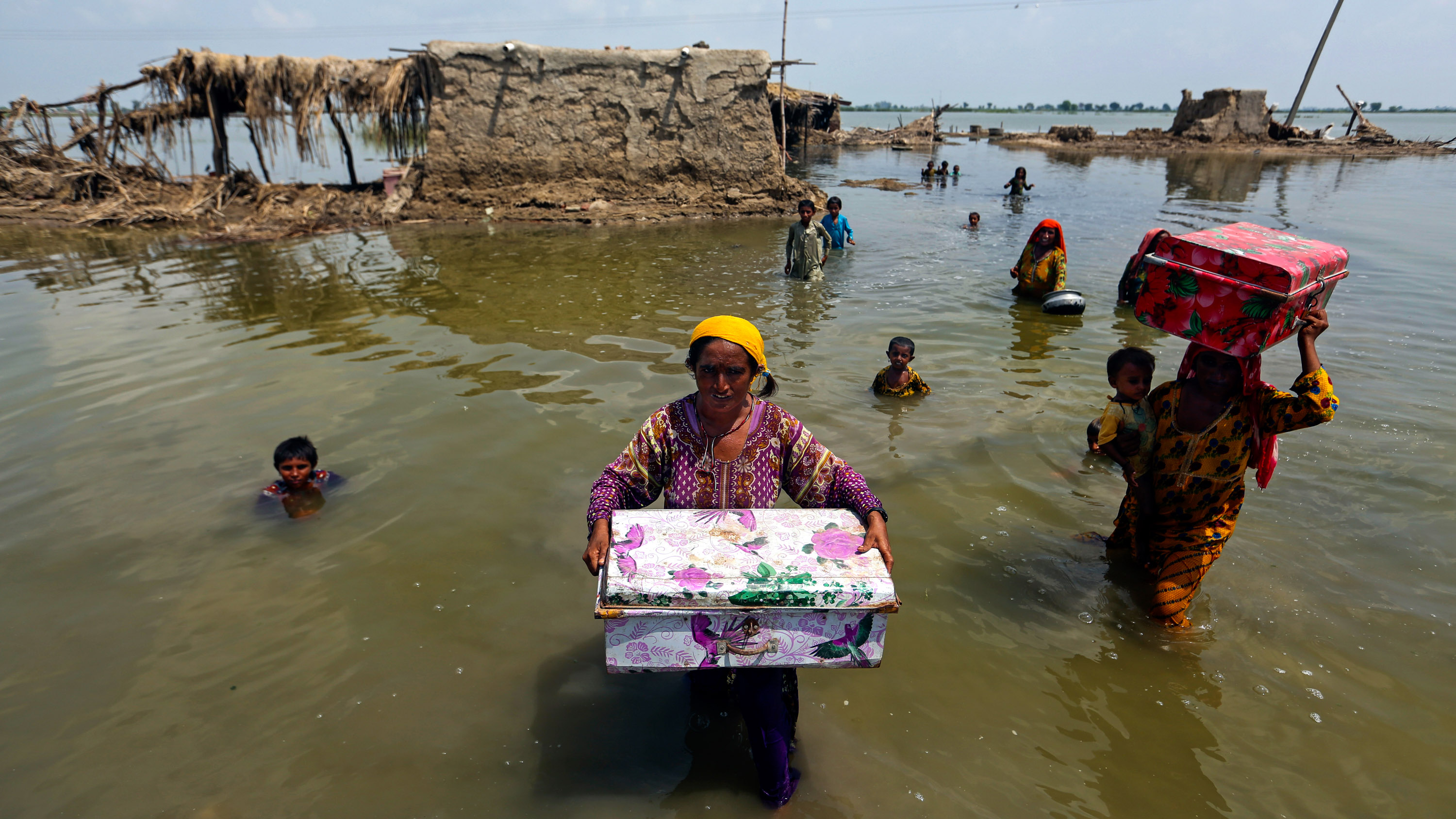 Pakistani women carry belongings salvaged from their flooded home after monsoon rains