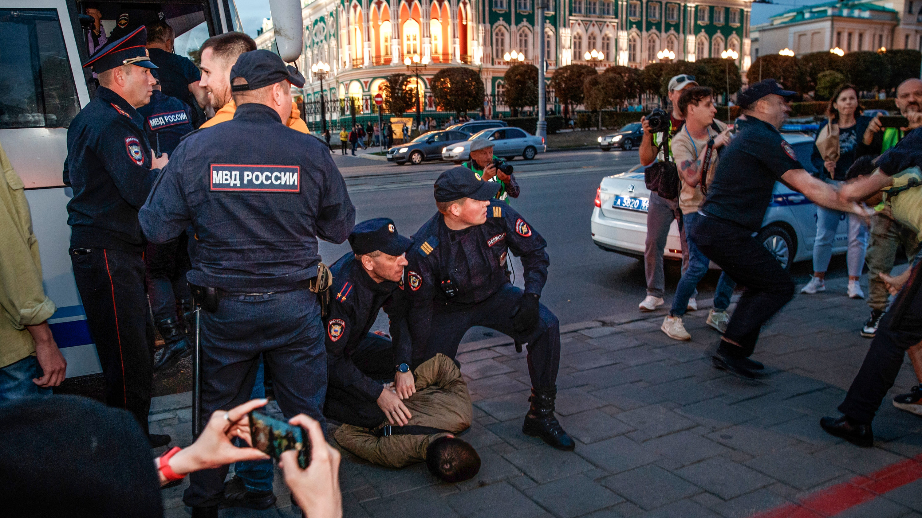 Police detain demonstrators during a protest against mobilization in Yekaterinburg, Russia while spectators record on cameras and phones.