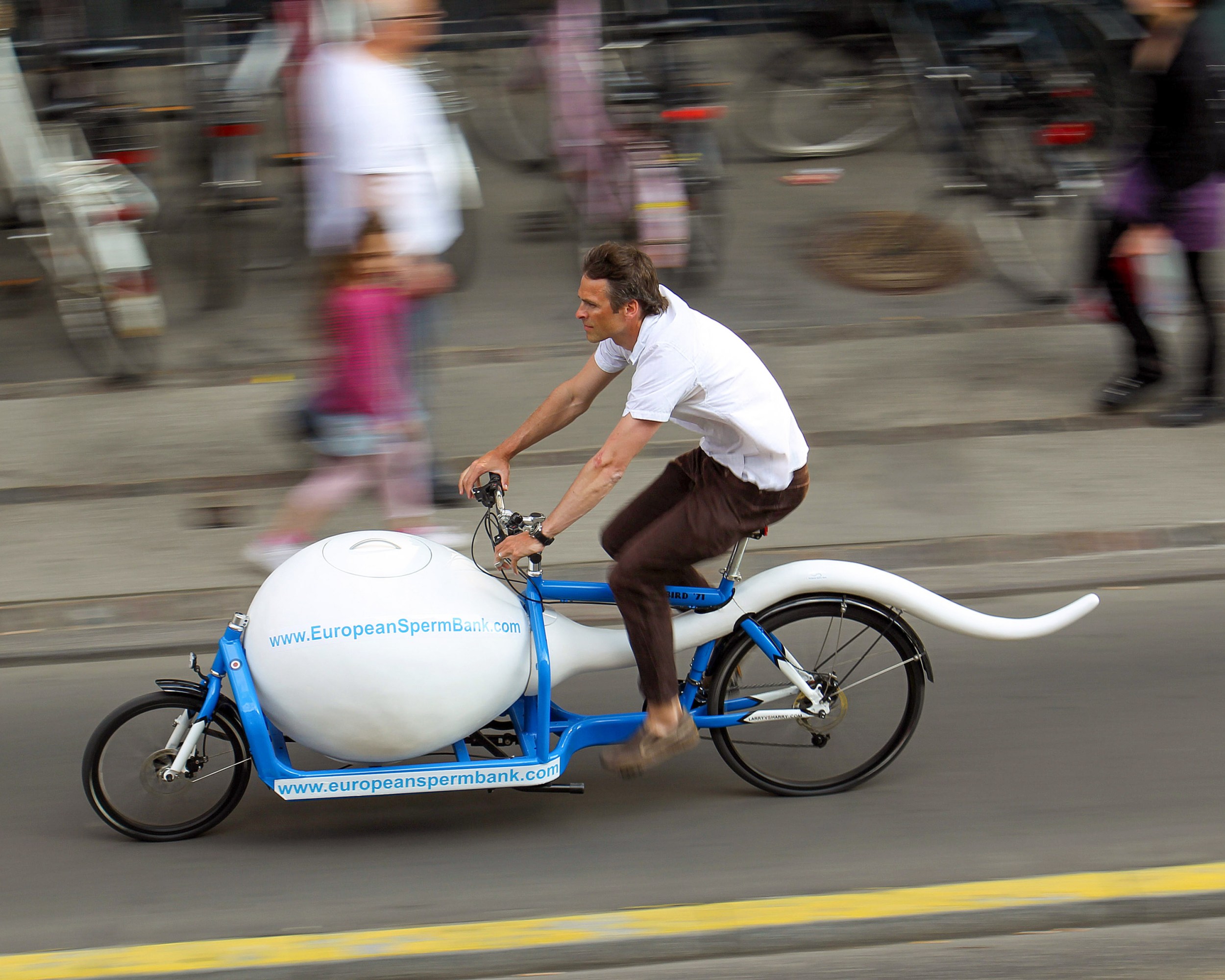 Courier on a bicycle shaped like sperm accelerating on the road
