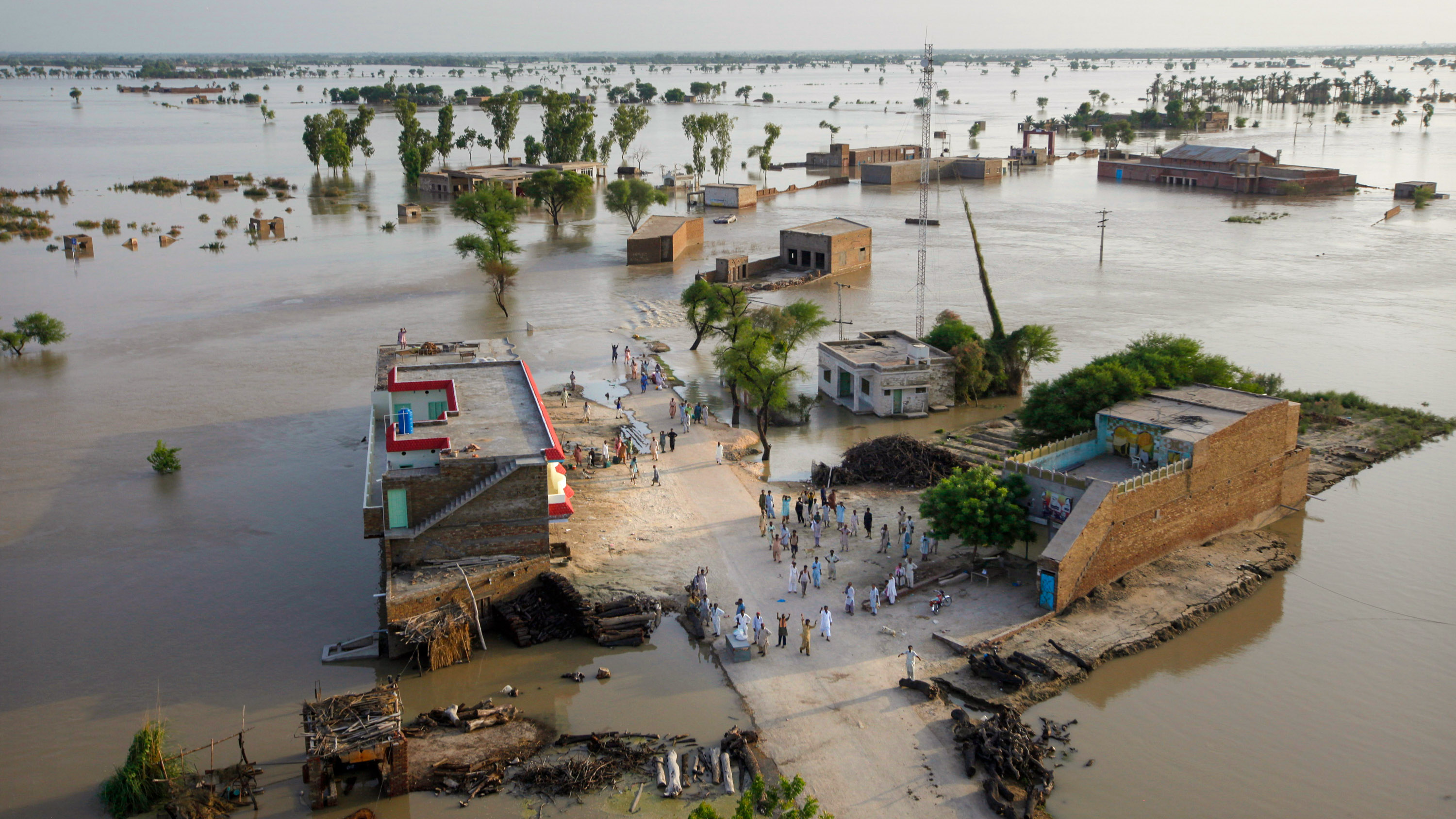 wide shot from a helicopter of a flooded village in Pakistan.  Stranded people waved for help from a dry place.