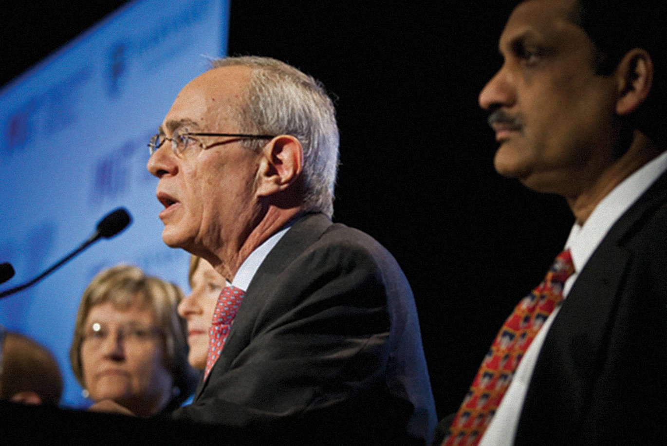 Reif speaking on stage with other panelists in frame