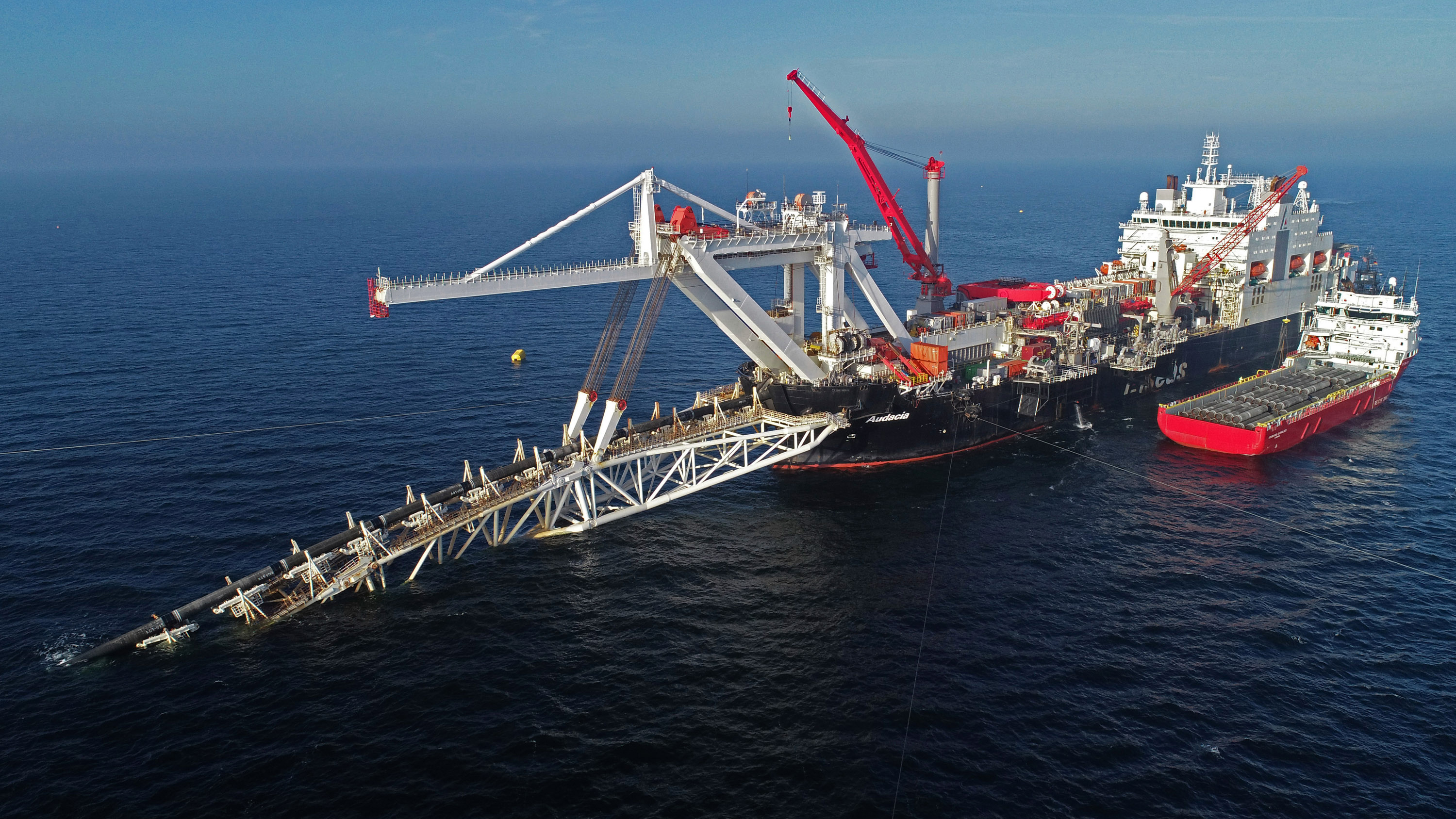 A ship at sea with cranes lowers sections of pipe into the water