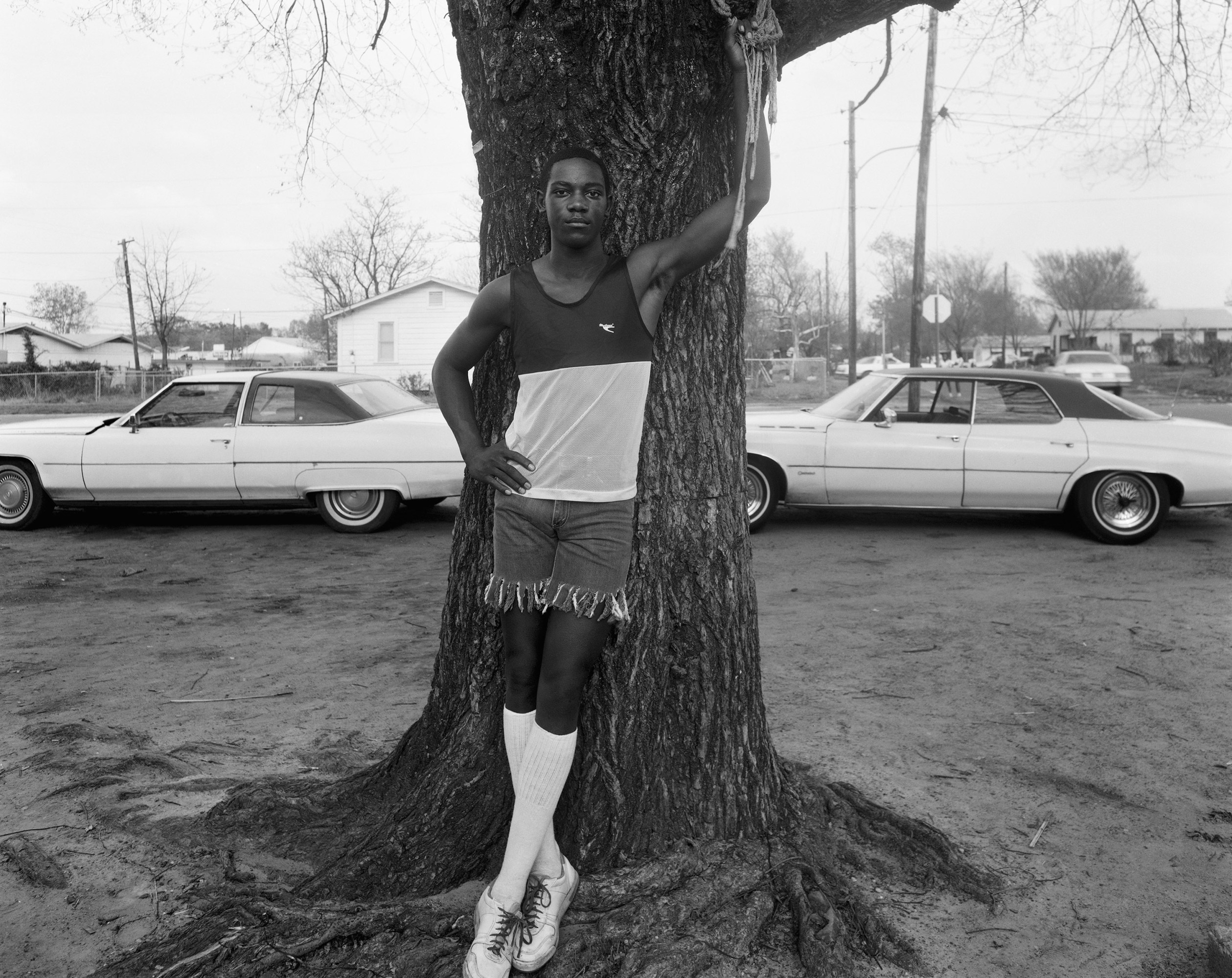 young man leaning against a tree in cut off shorts and tall socks