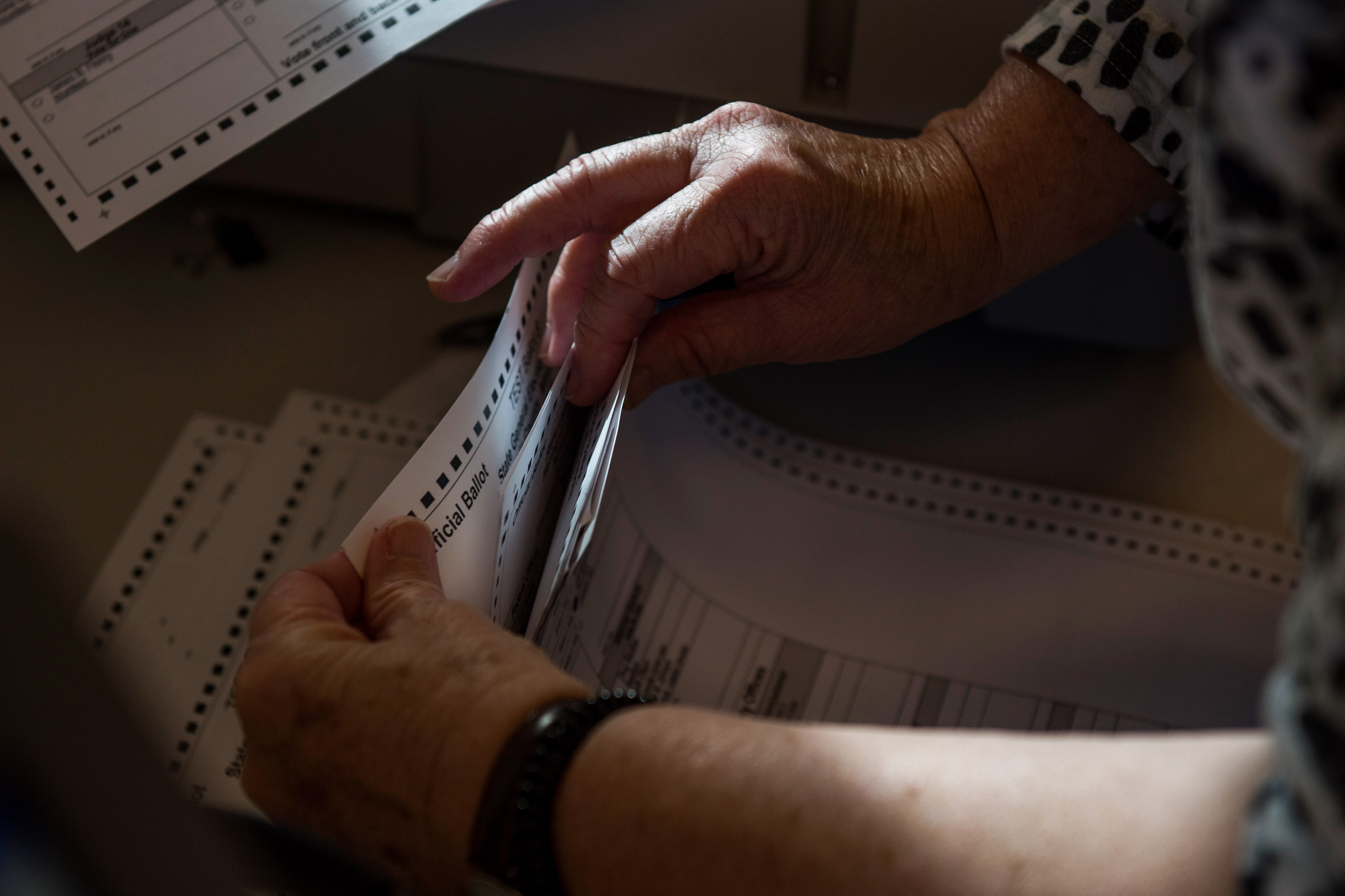 Hands of an election official conducting a count of paper test ballots.