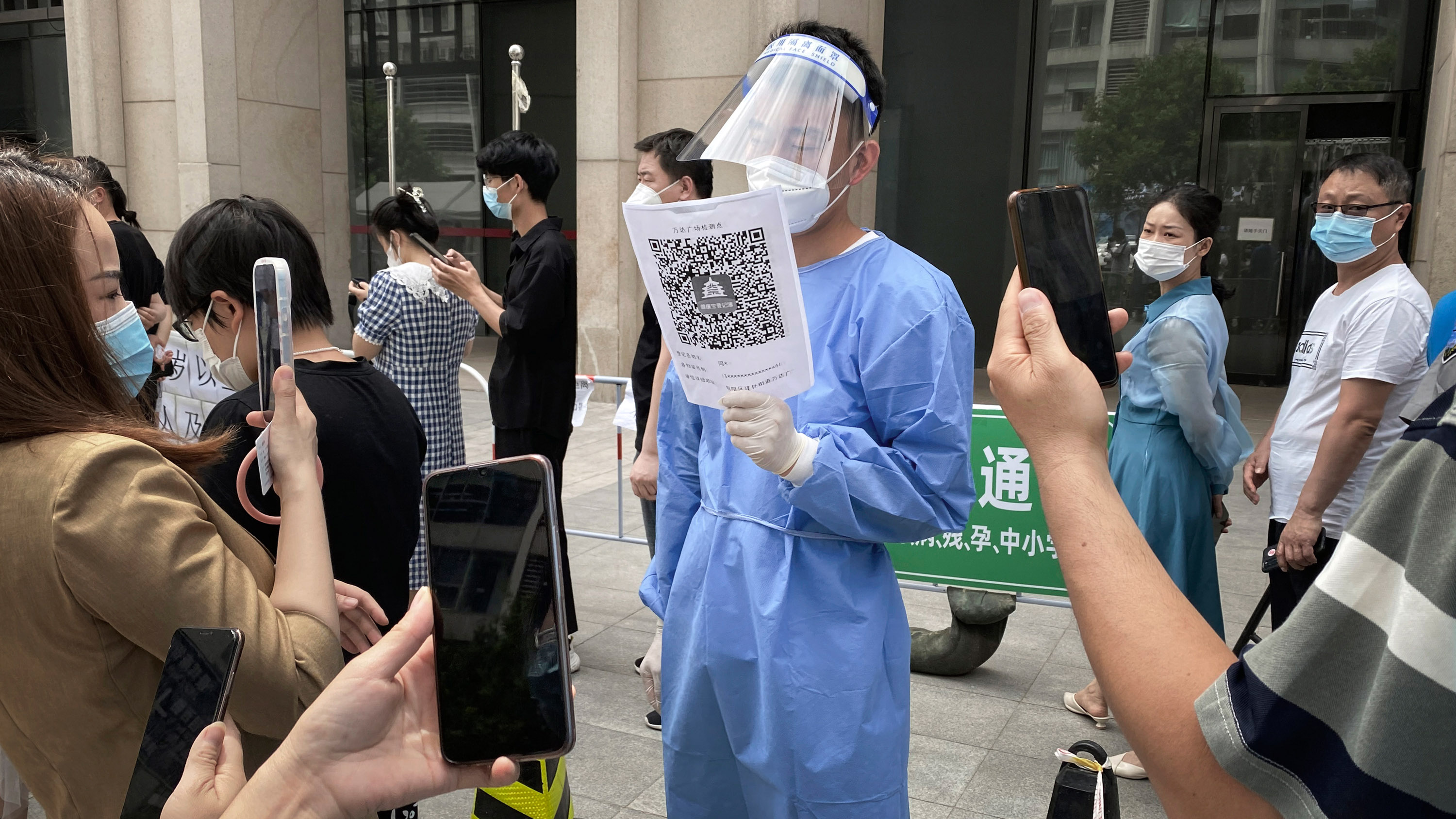 A health worker holds a Beijing Health Code for people to scan as they line up for a covid test