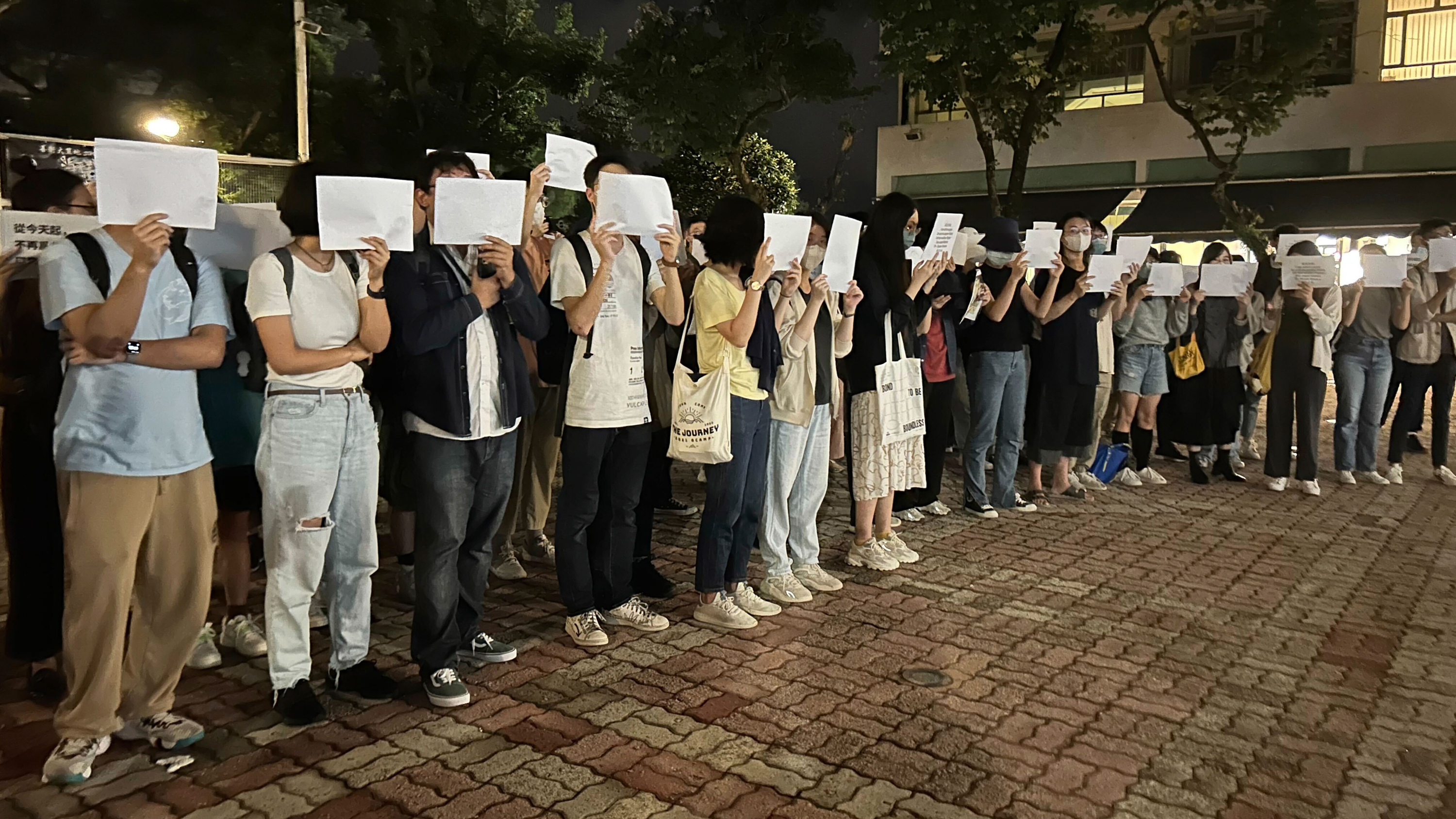 A line of student protestors in Hong Kong hold a white piece of paper over their faces.