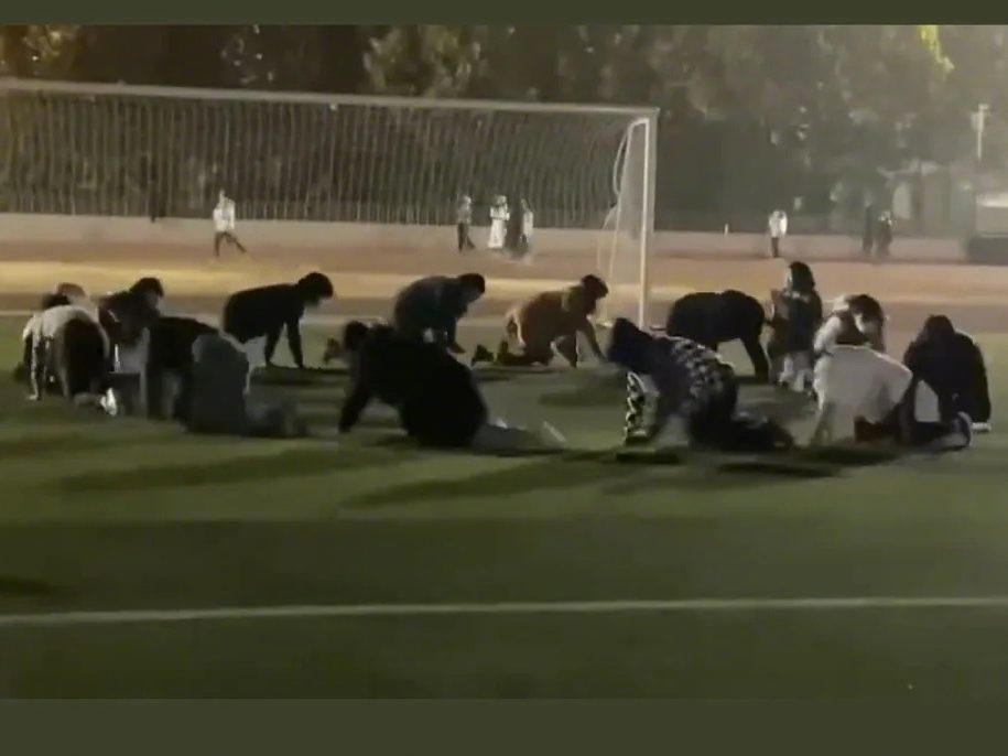 A photo of a dozen students crawling in a circle on a soccer field at night.