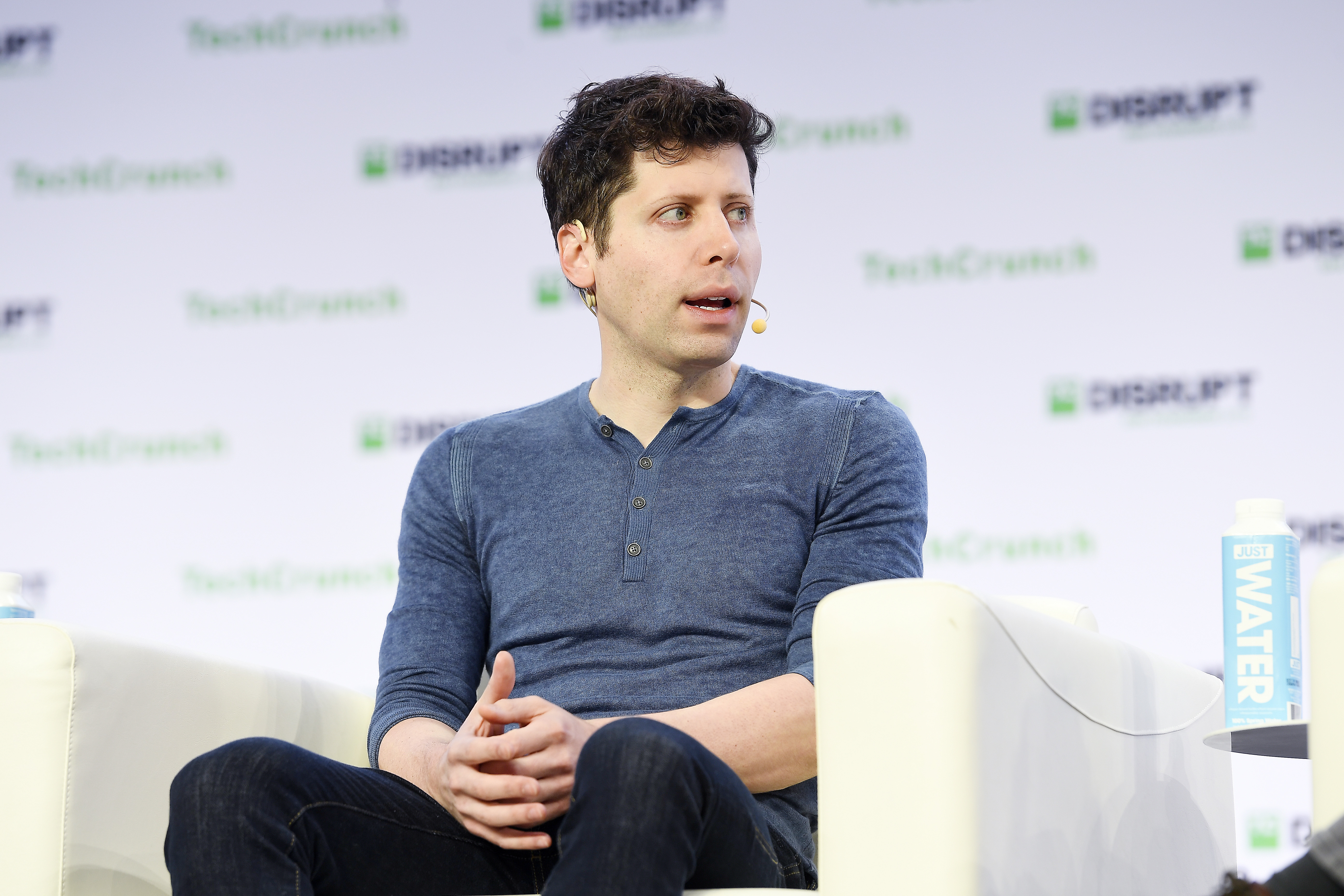 A photo of Sam Altman sitting in a chair on a stage