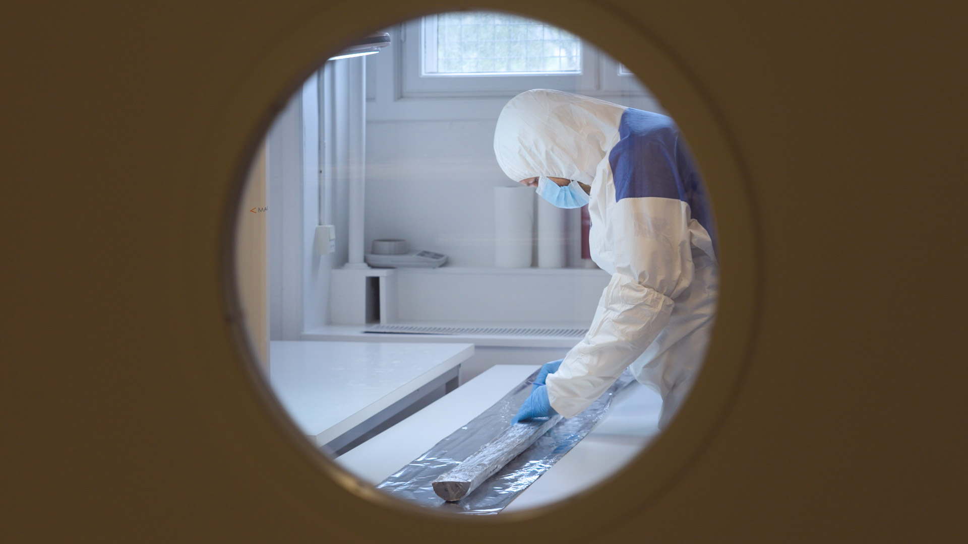 a scientist looking at a sample in a clean room, seen through a round window in the door