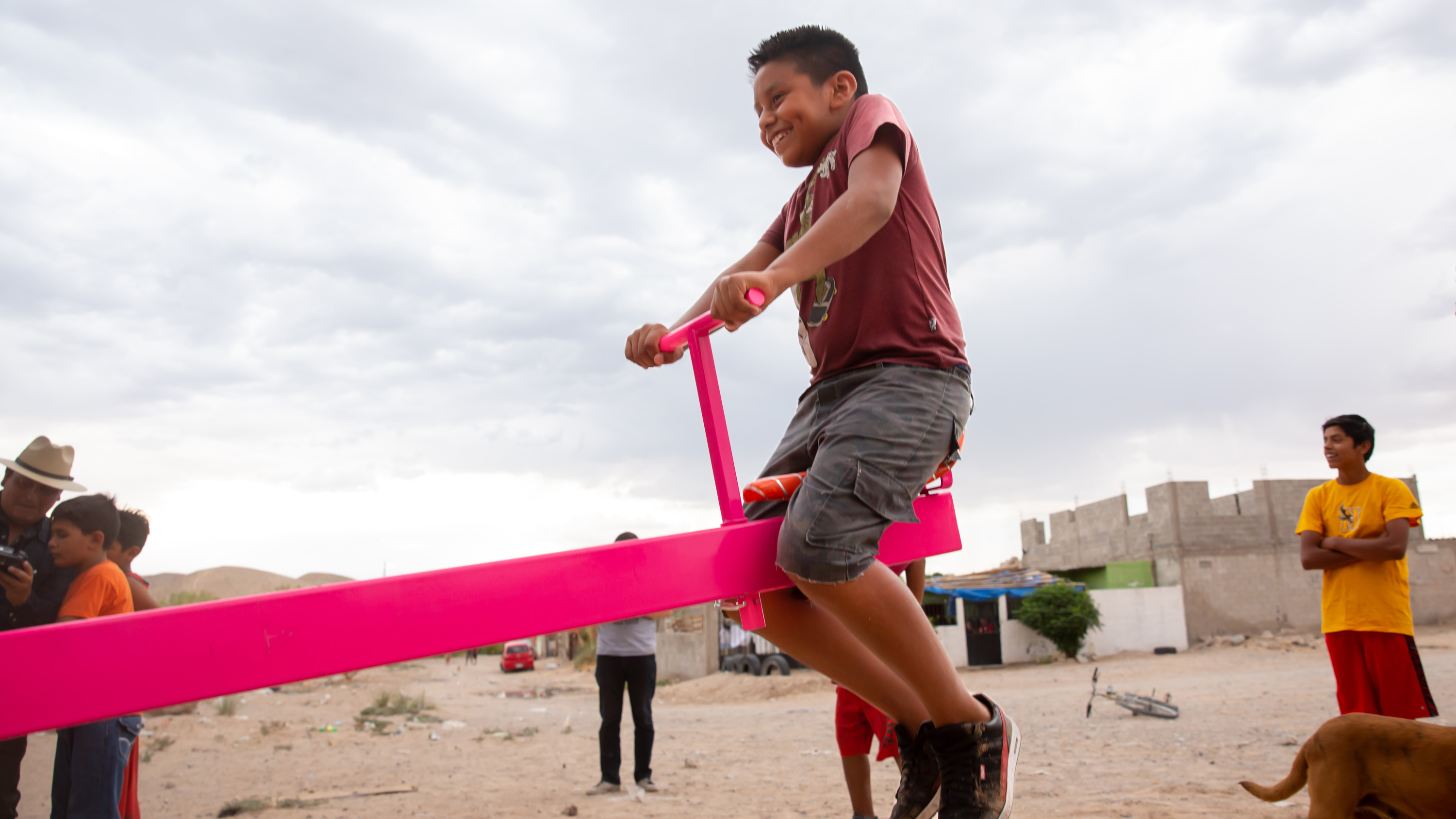 child on a pink teeter-totter installed on the US-Mexico border wall