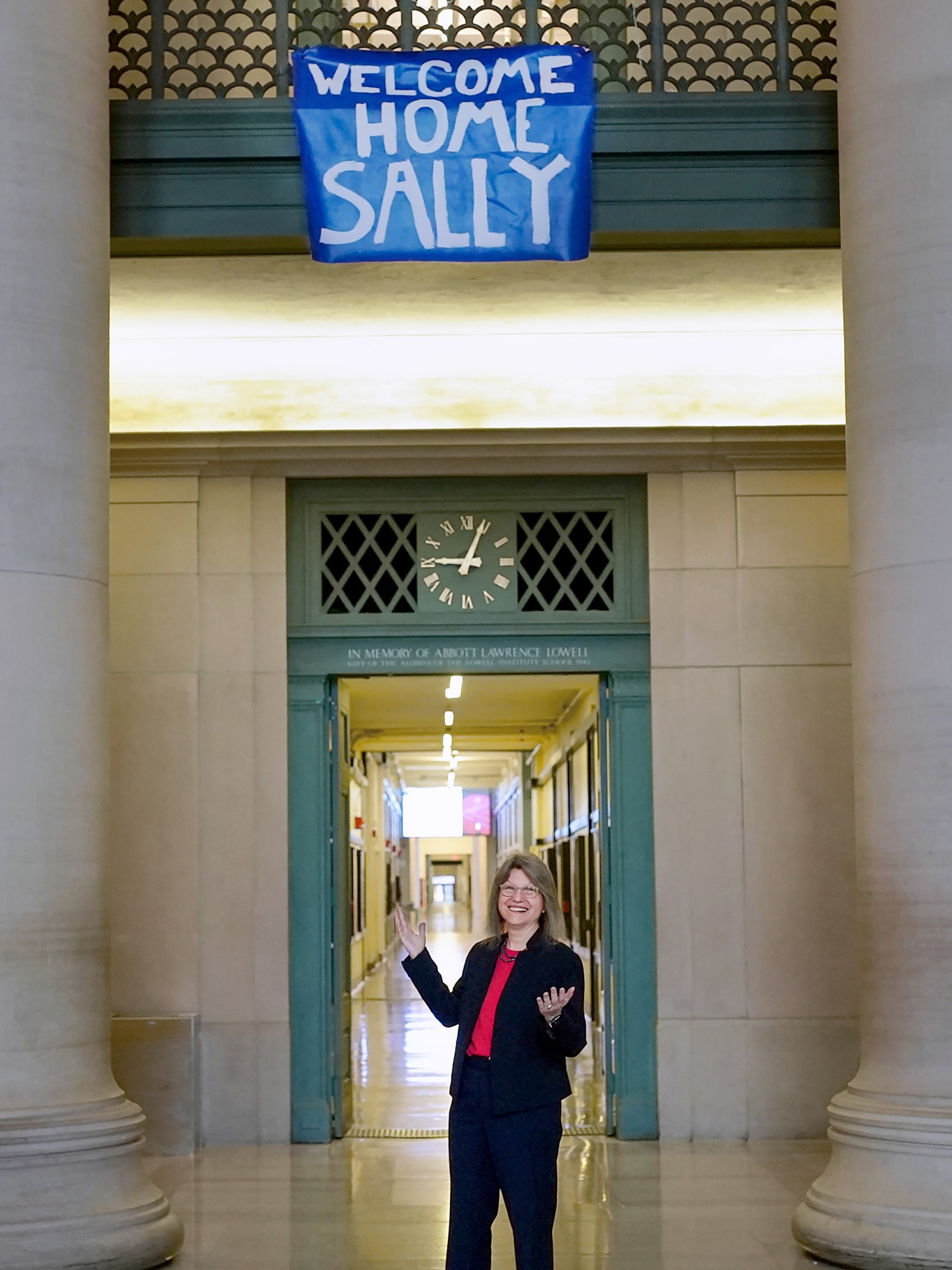 Sally Kornbluth stands under a "Welcome Home Sally" banner in Lobby 7