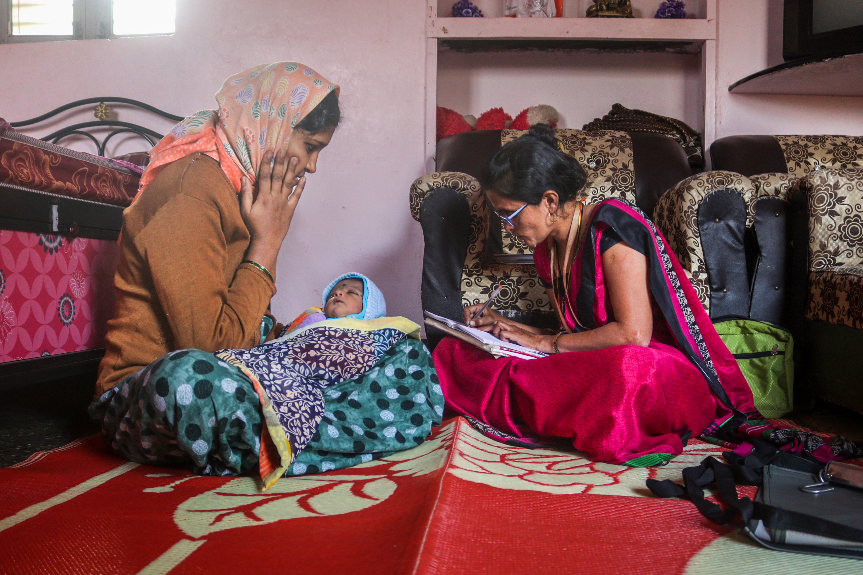 Maya Patil taking case notes with a mother and child in her home
