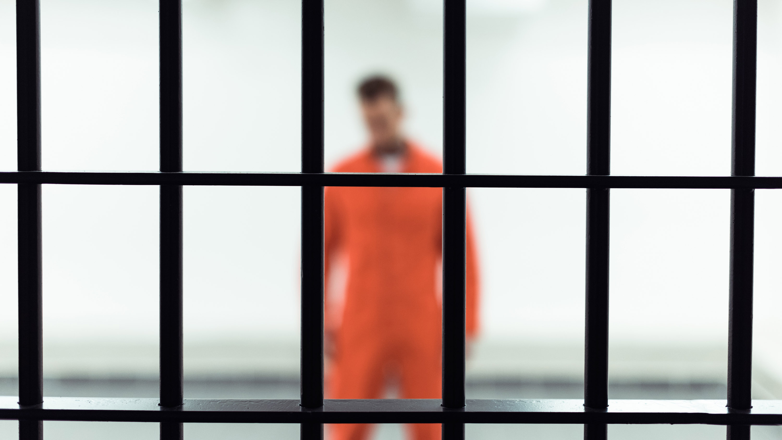 man in orange prison jumpsuit out of focus behind metal bars