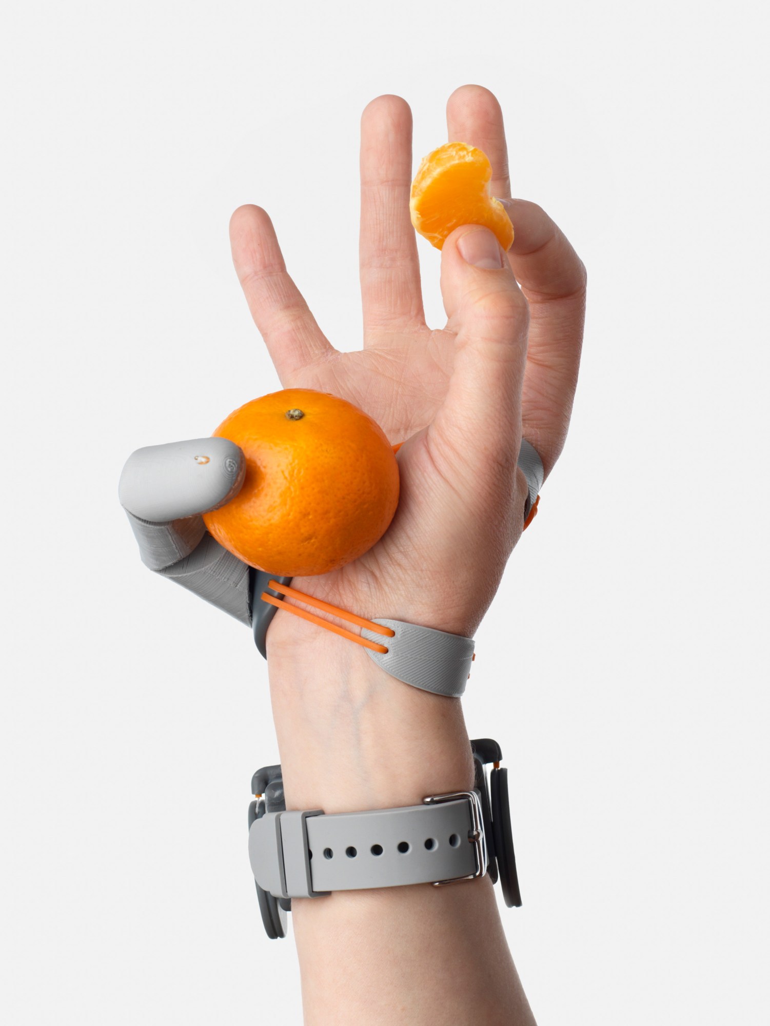 prosthetic finger holds a clementine against the palm of a hand, while a single segment is held by the forefinger and thumb