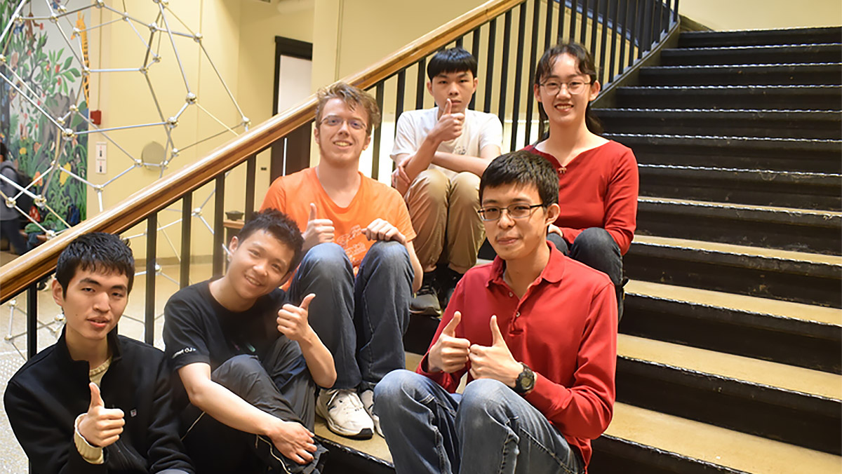 Six students sit on stairway and give the thumbs up