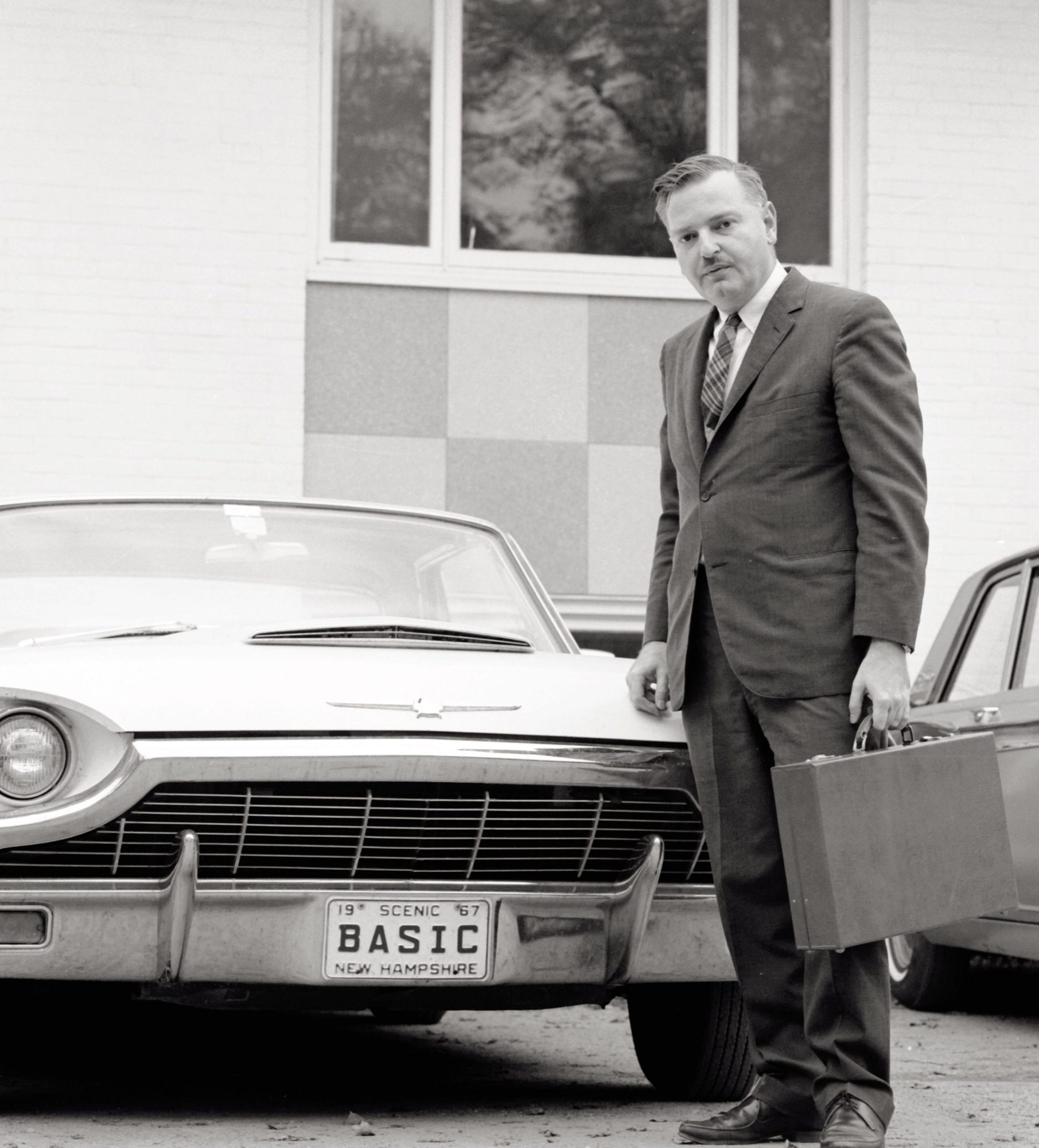 John Kemeny standing in a parking lot by a car with the New Hampshire vanity plate "BASIC"