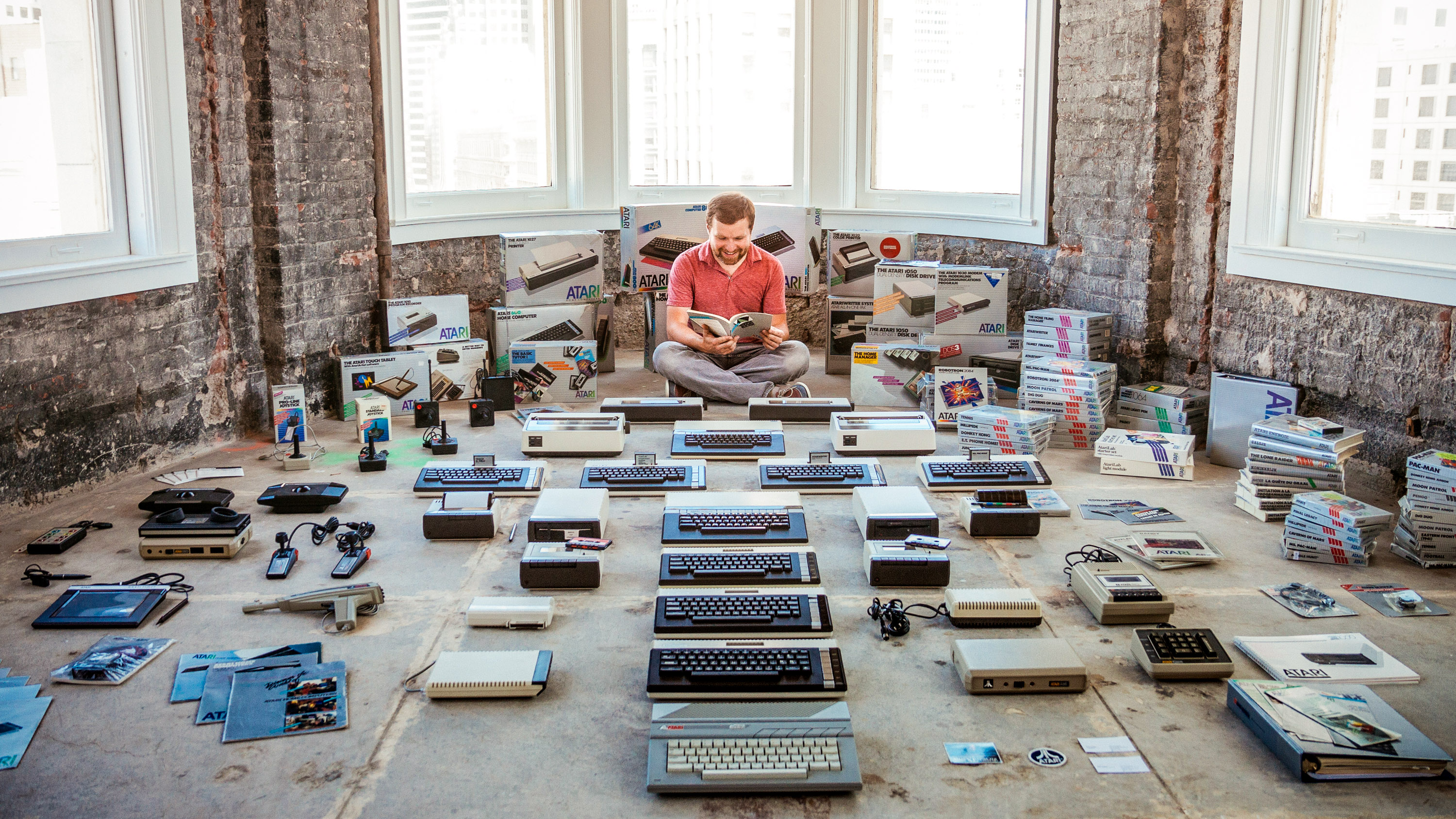 Marcin Wichary sitting on the floor surrounded by his collection of keyboards.