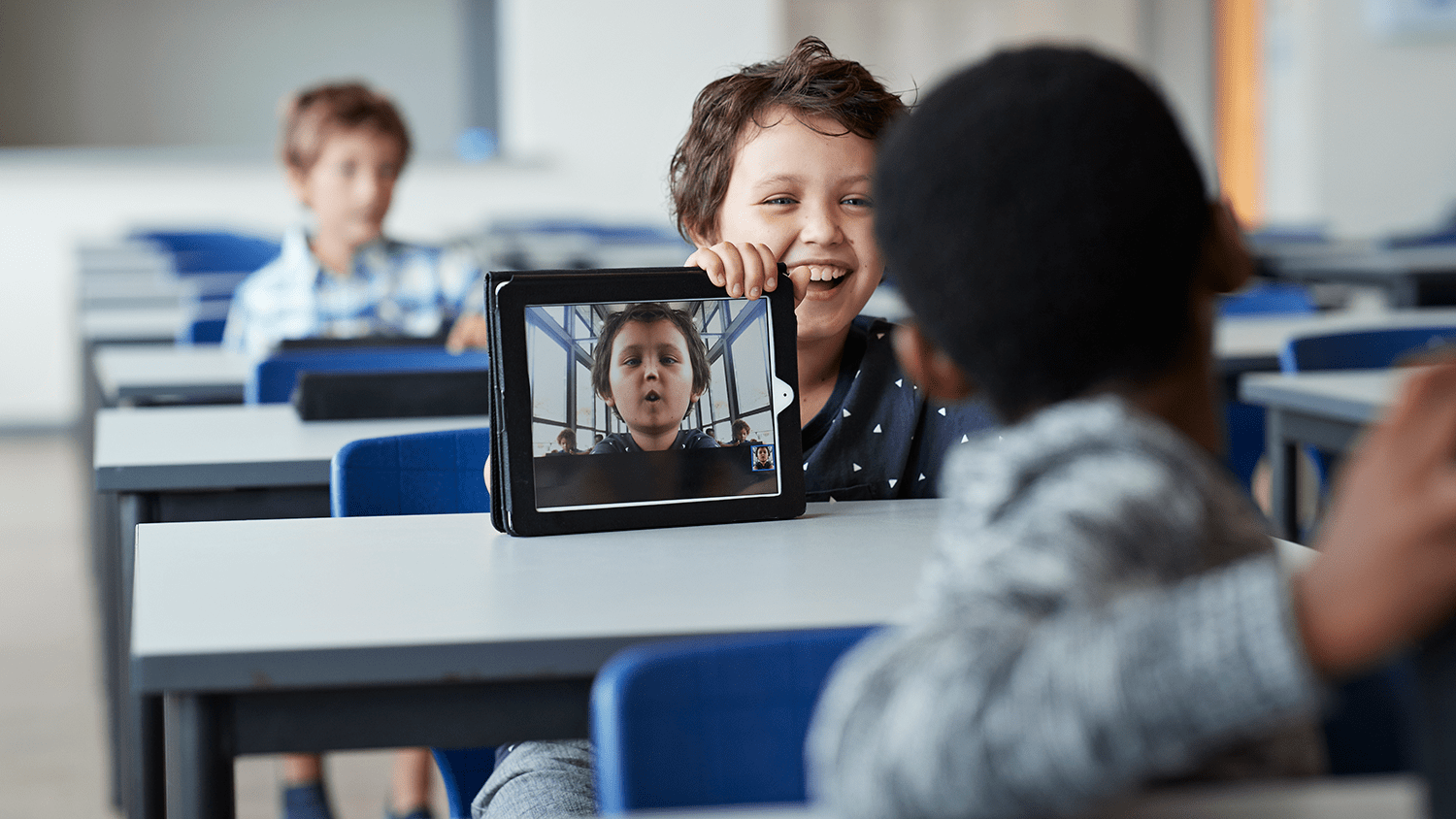 stock image of kids in a classroom with a tablet showing goofy selfies