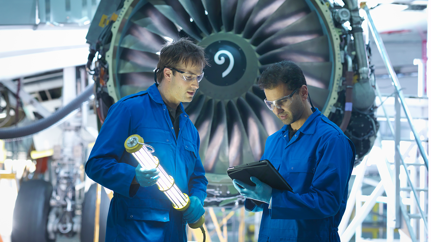 Imagen de stock de dos científicos en un taller mecánico revisando información en una tableta