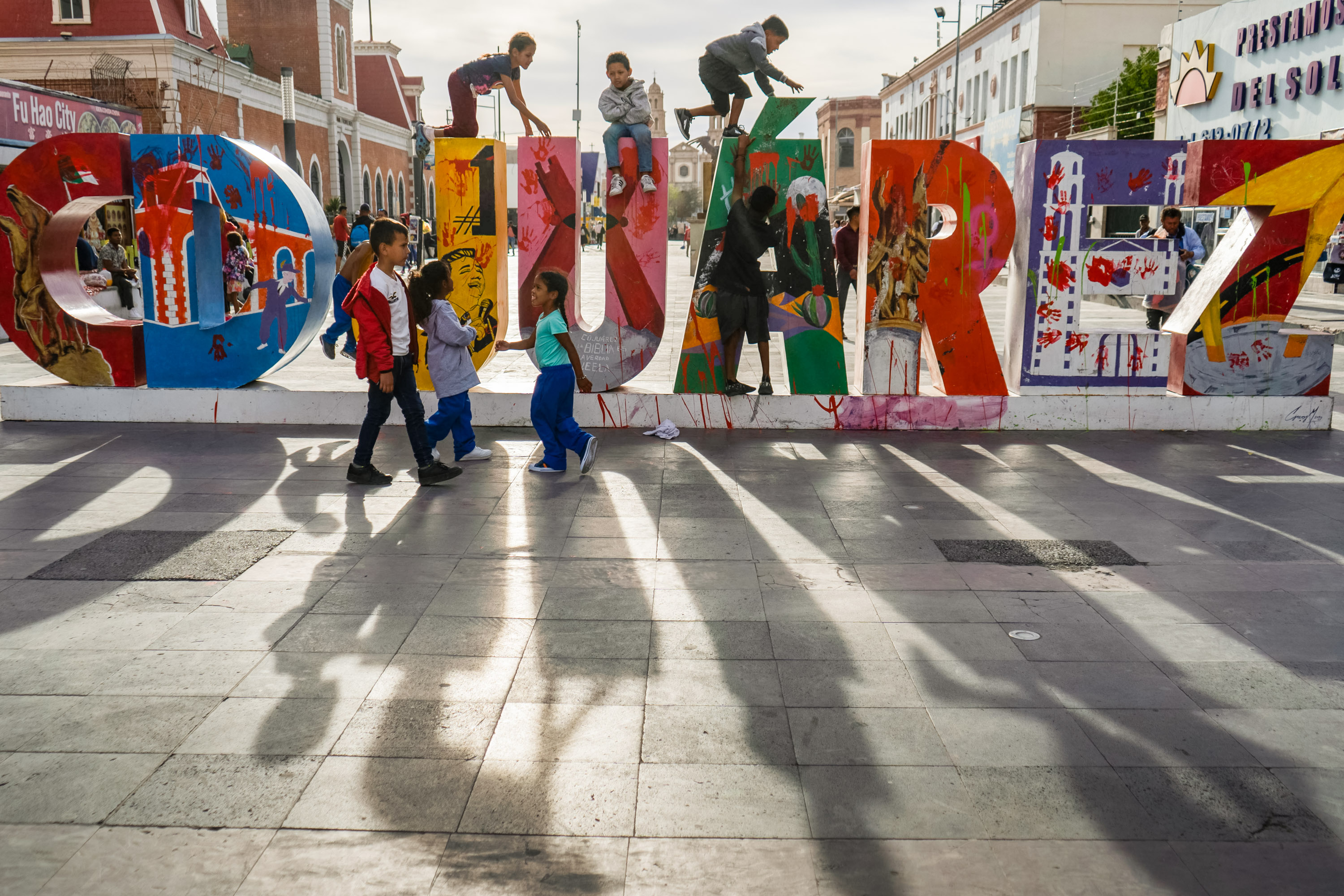 niños se suben a una escultura tridimensional de la obra Juárez. El sol hace largas sombras en primer plano.