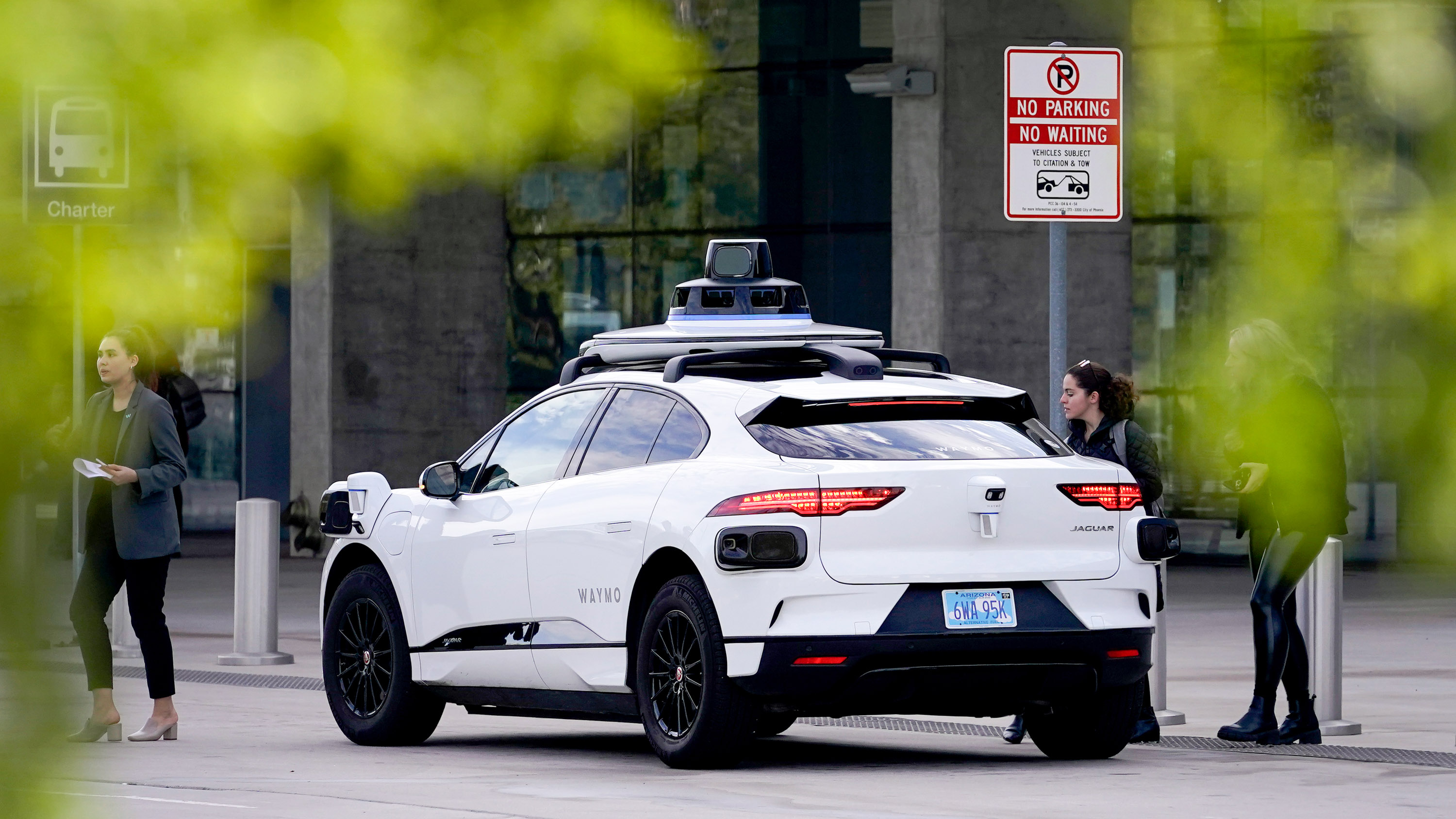 A Waymo self-driving vehicle sits curbside as a woman approaches for a ride