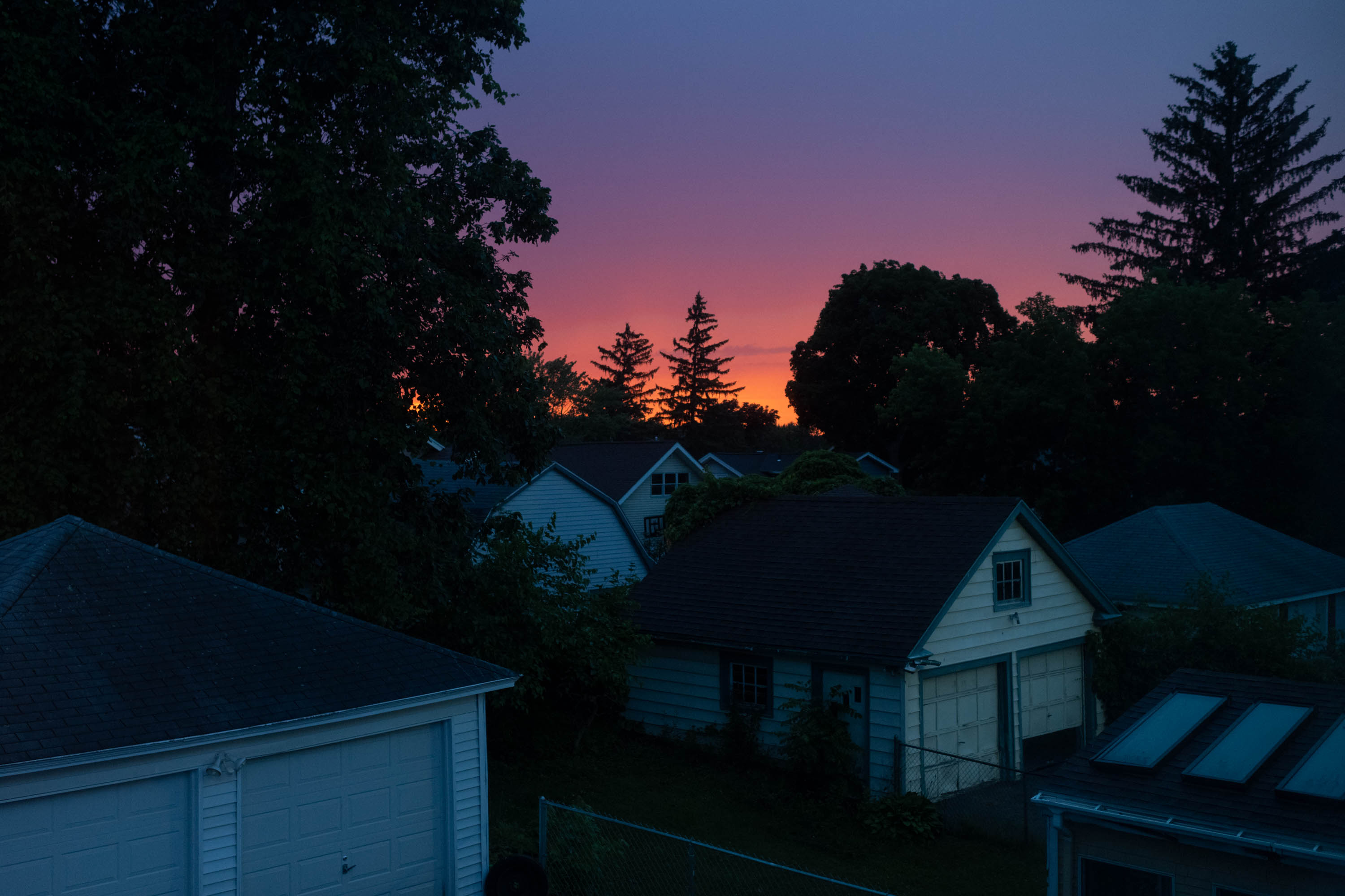 Se muestra una vibrante puesta de sol naranja, rosa y azul sobre un vecindario suburbano en Syracuse, Nueva York.