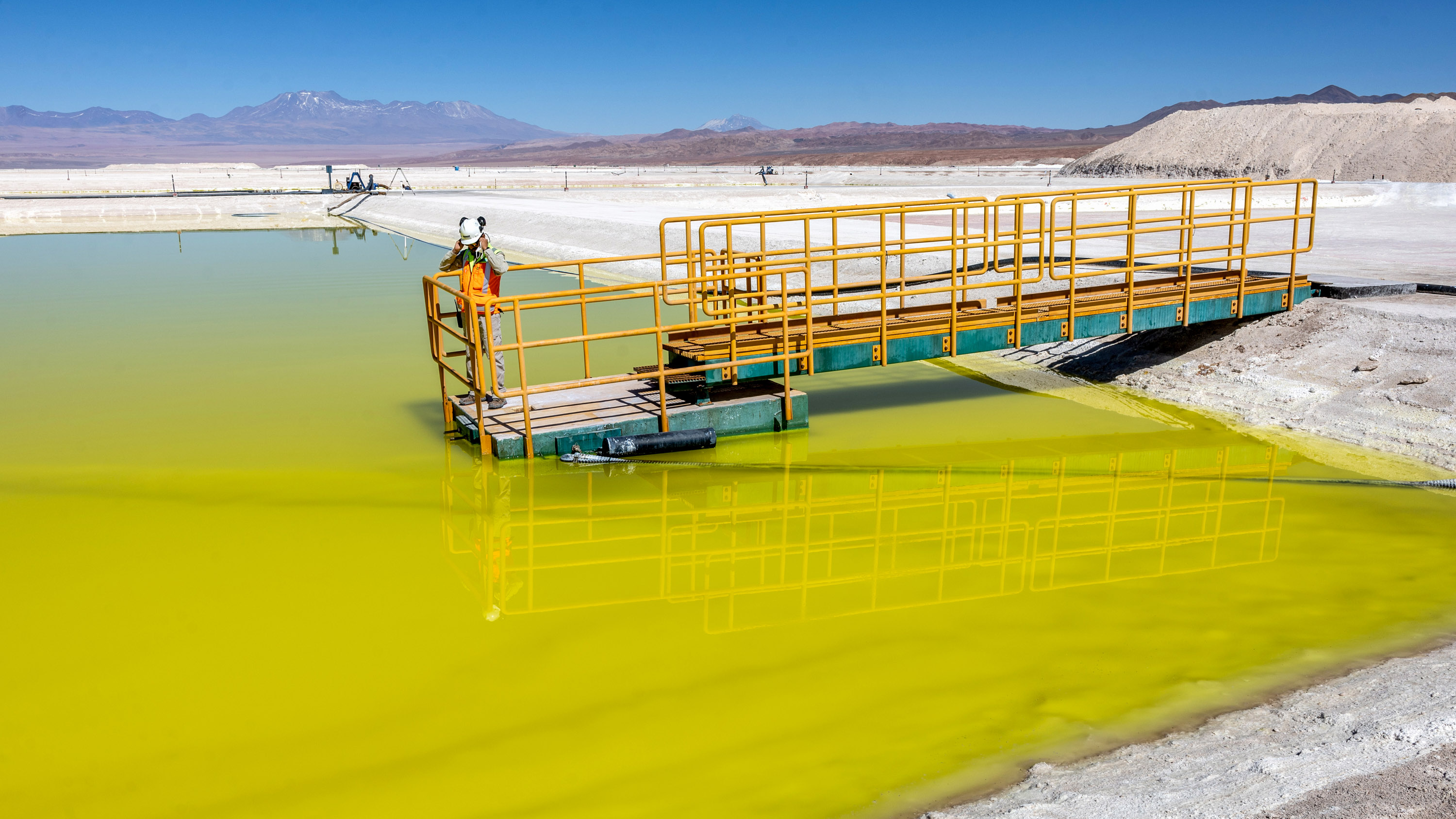 A lithium mine supervisor stands on a gangplank to inspect an evaporation pond of yellow lithium-rich brine