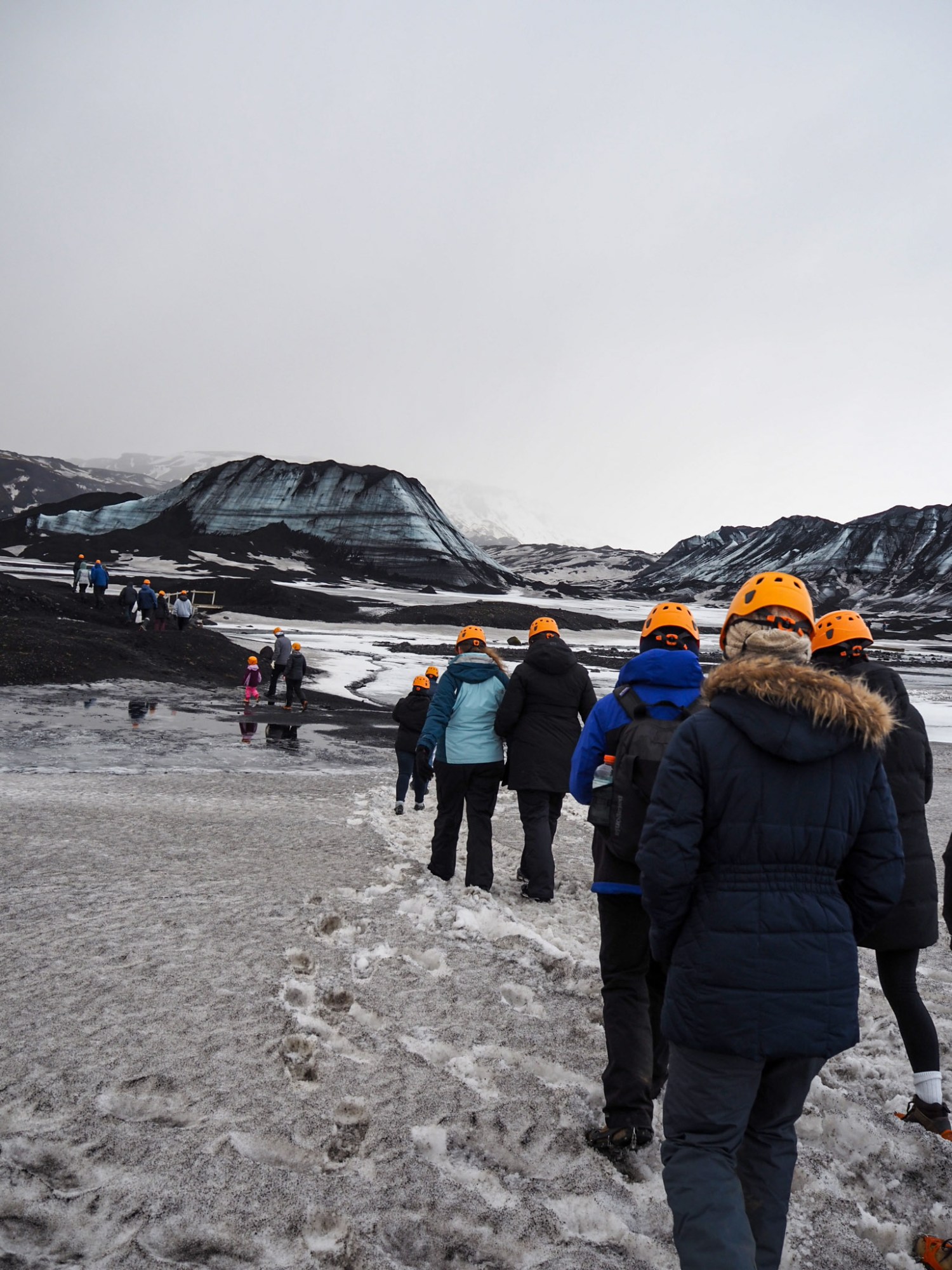 a line of people in orange safety helmets hike across the icy landscape